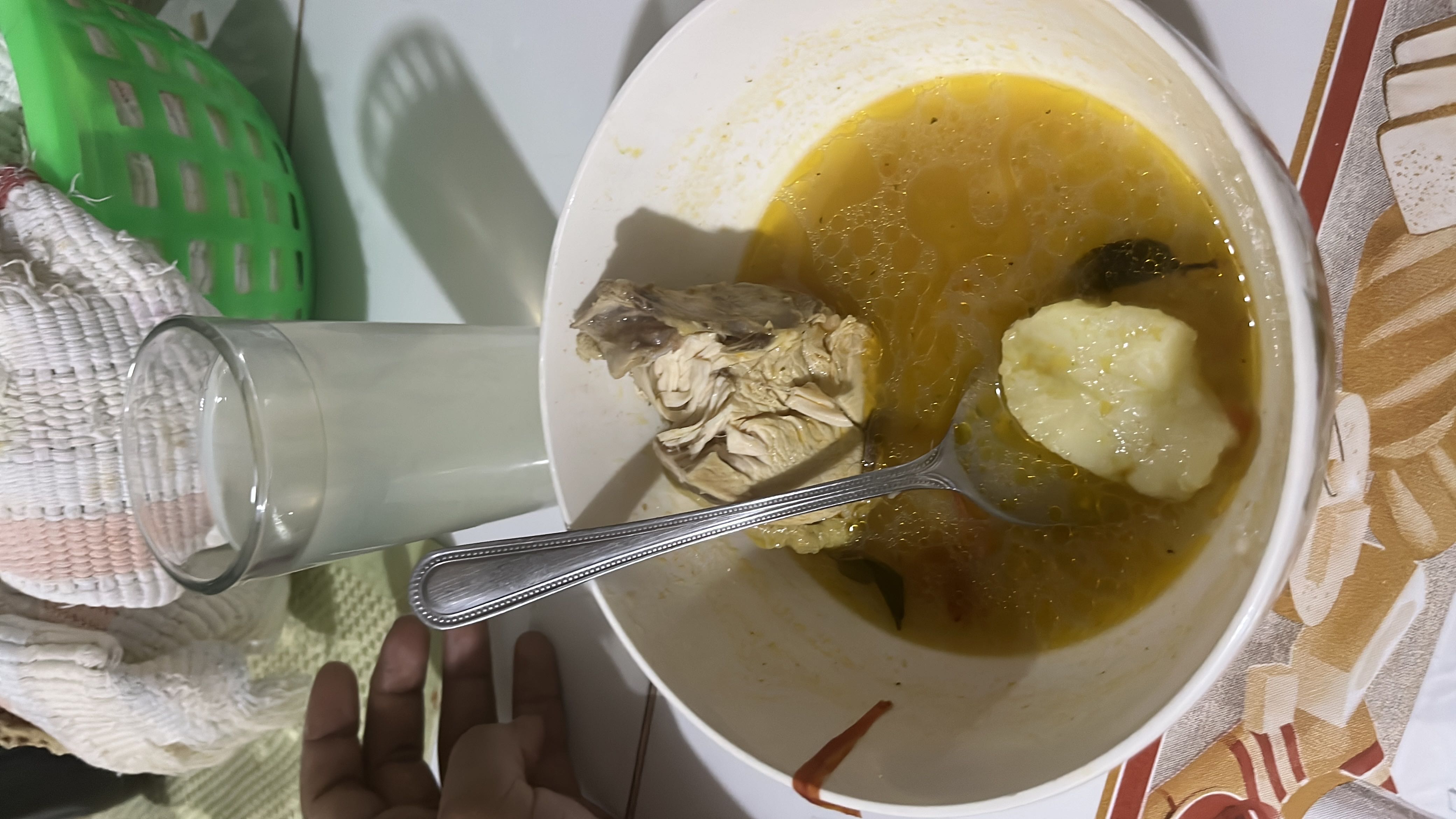 A bowl of chicken soup with a piece of chicken, potato, and broth, accompanied by a glass of a light beverage.
