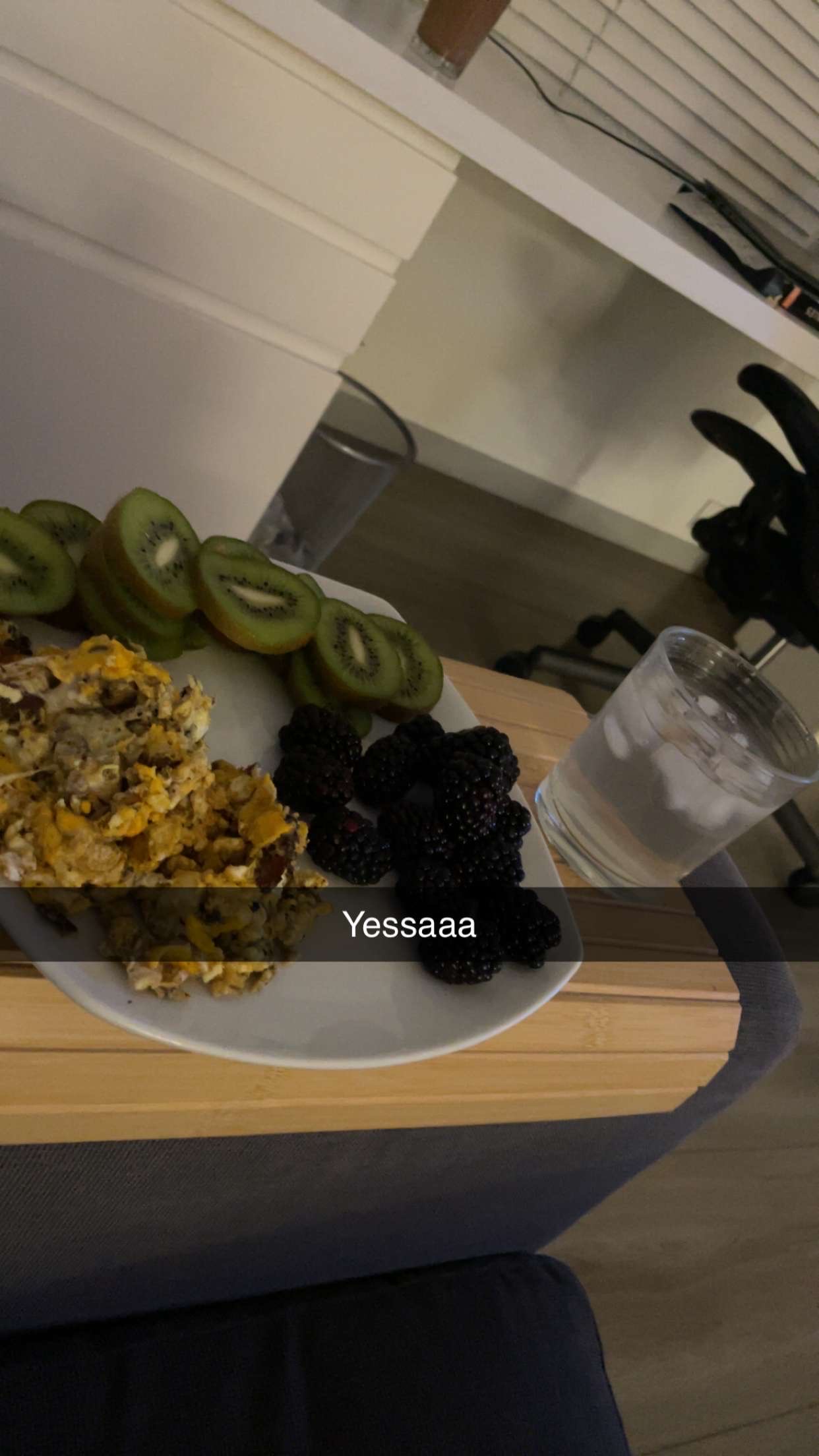A healthy meal consisting of sliced kiwi, blackberries, and scrambled eggs, served with a glass of water.