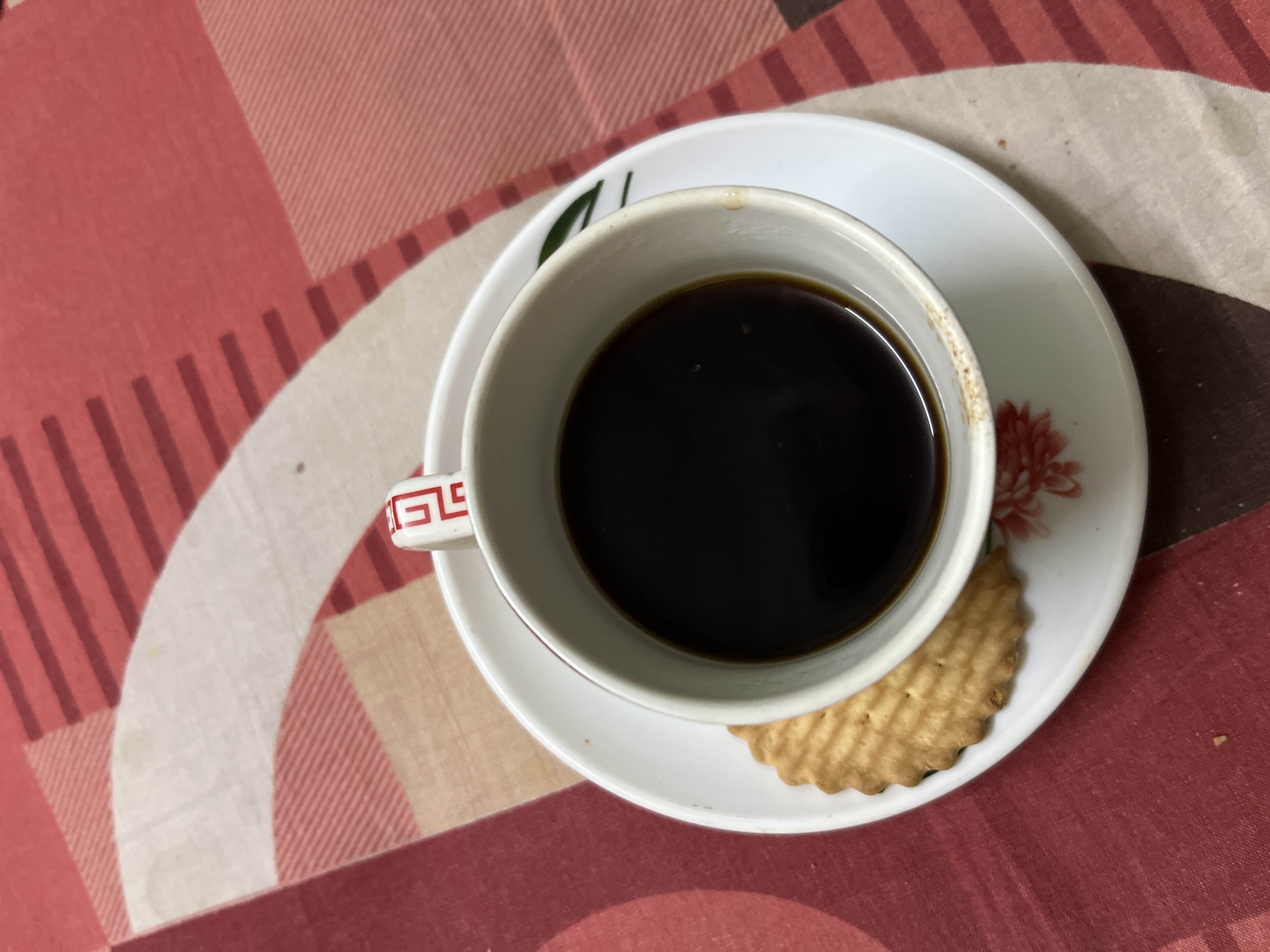 A cup of black coffee served with a single biscuit, providing a light snack with minimal calories.