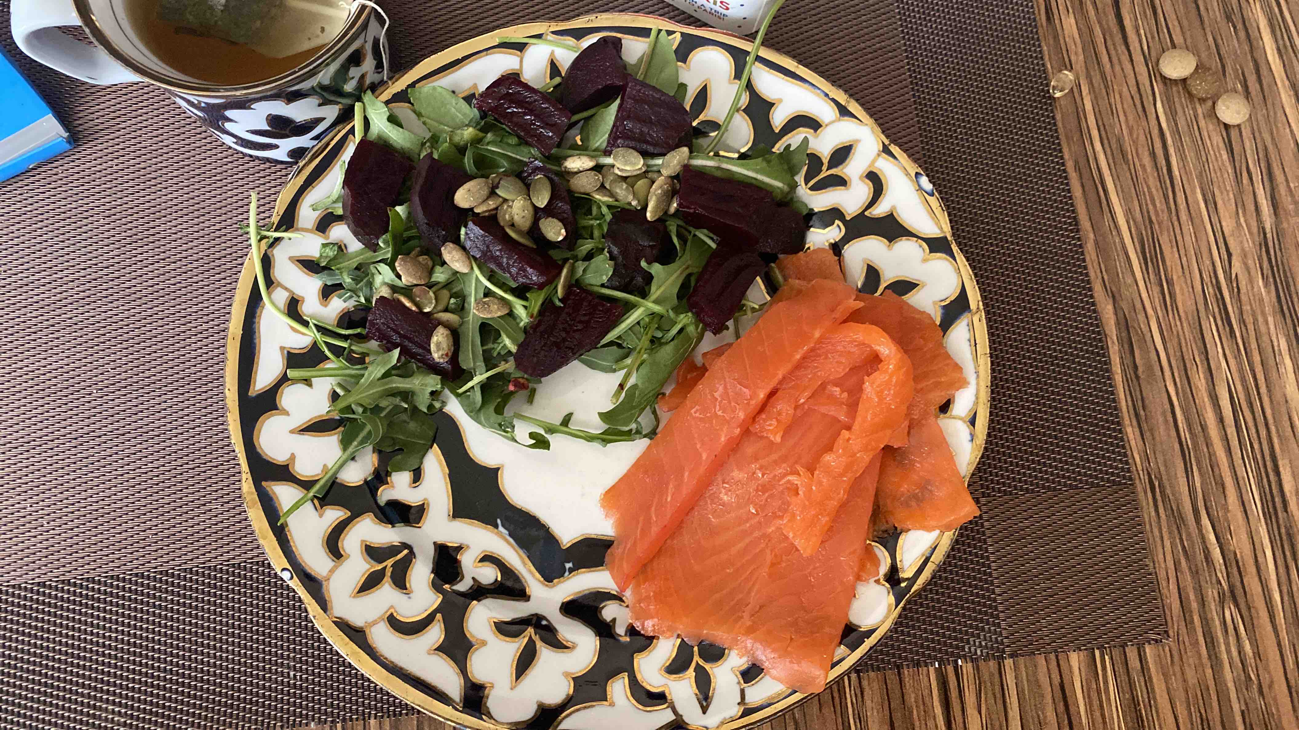 A healthy plate featuring smoked salmon, arugula, roasted beets, and pumpkin seeds, served with a cup of tea.