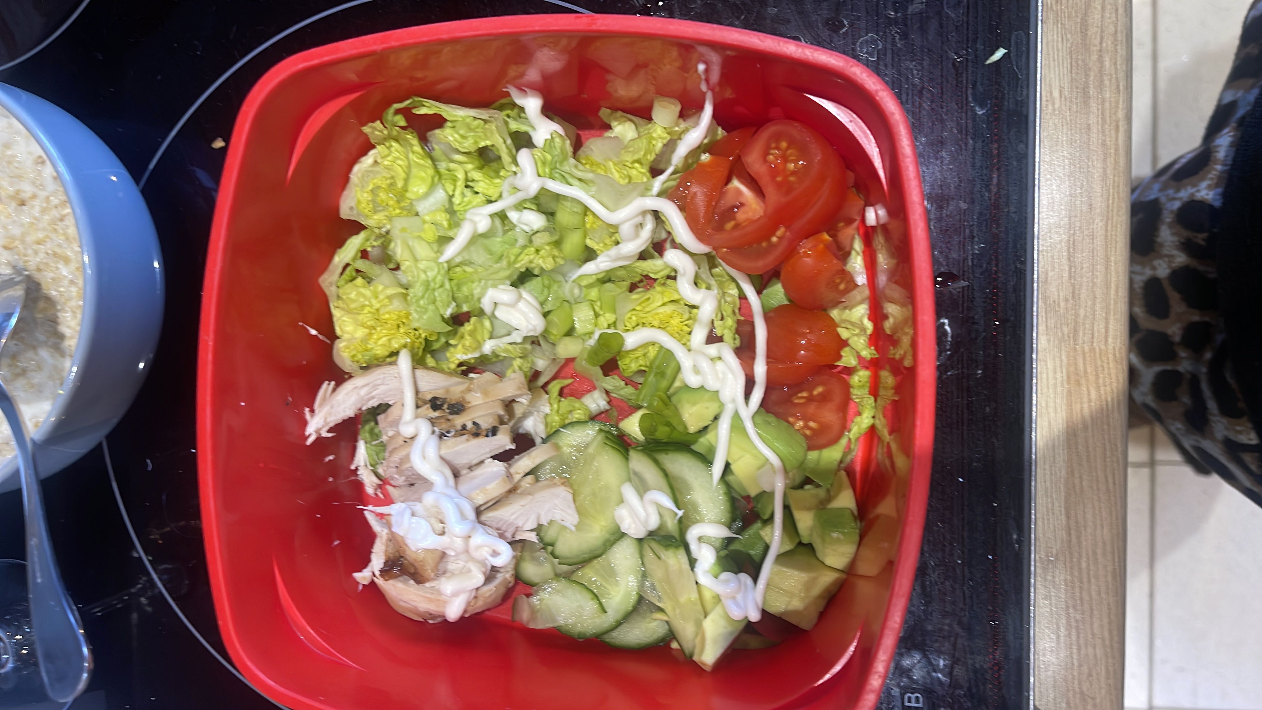 A healthy salad containing chicken, lettuce, cucumber, avocado, cherry tomatoes, and mayonnaise.