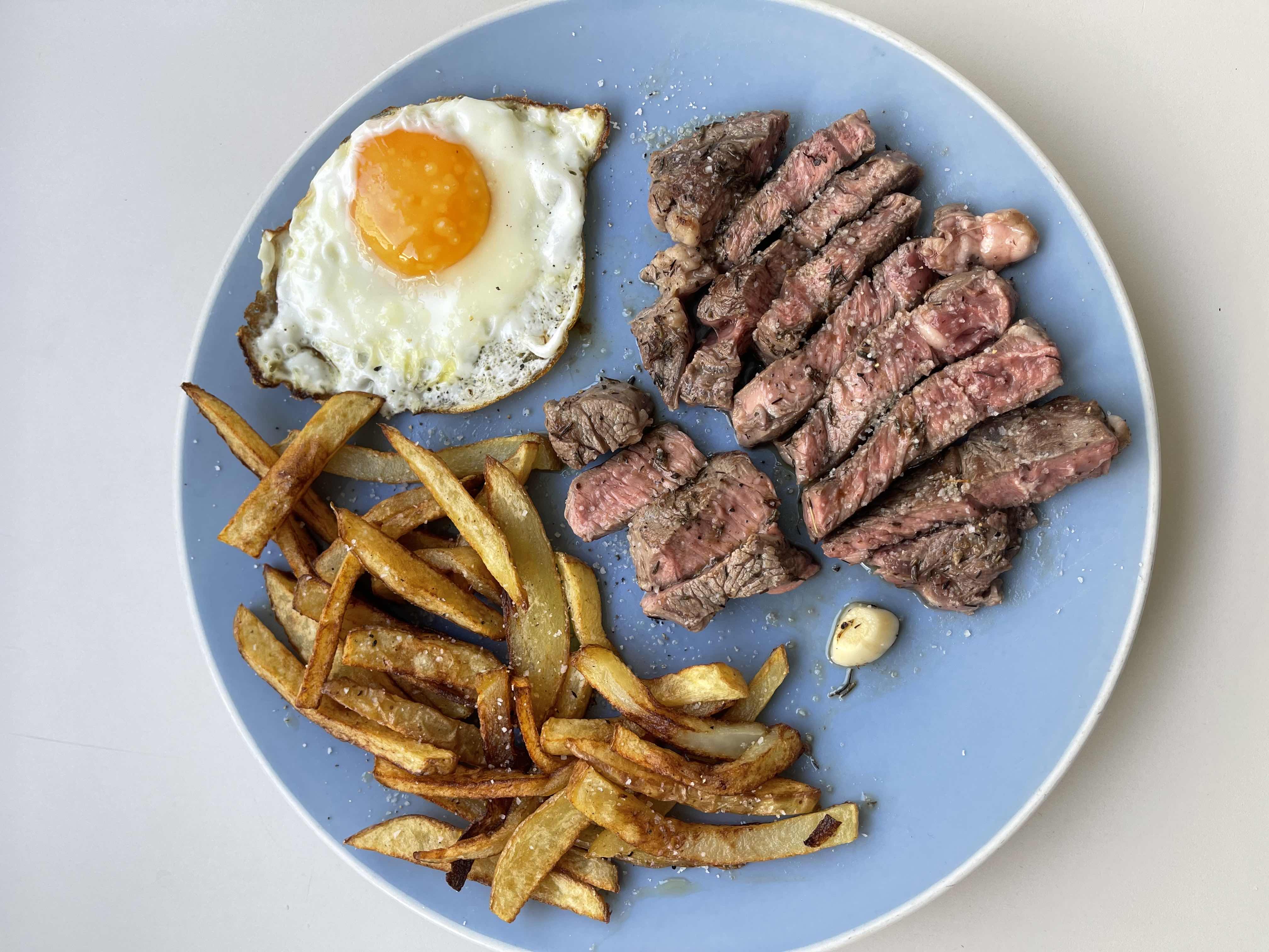 A balanced meal consisting of steak, a fried egg, and french fries, providing a mix of protein, fats, and carbohydrates.