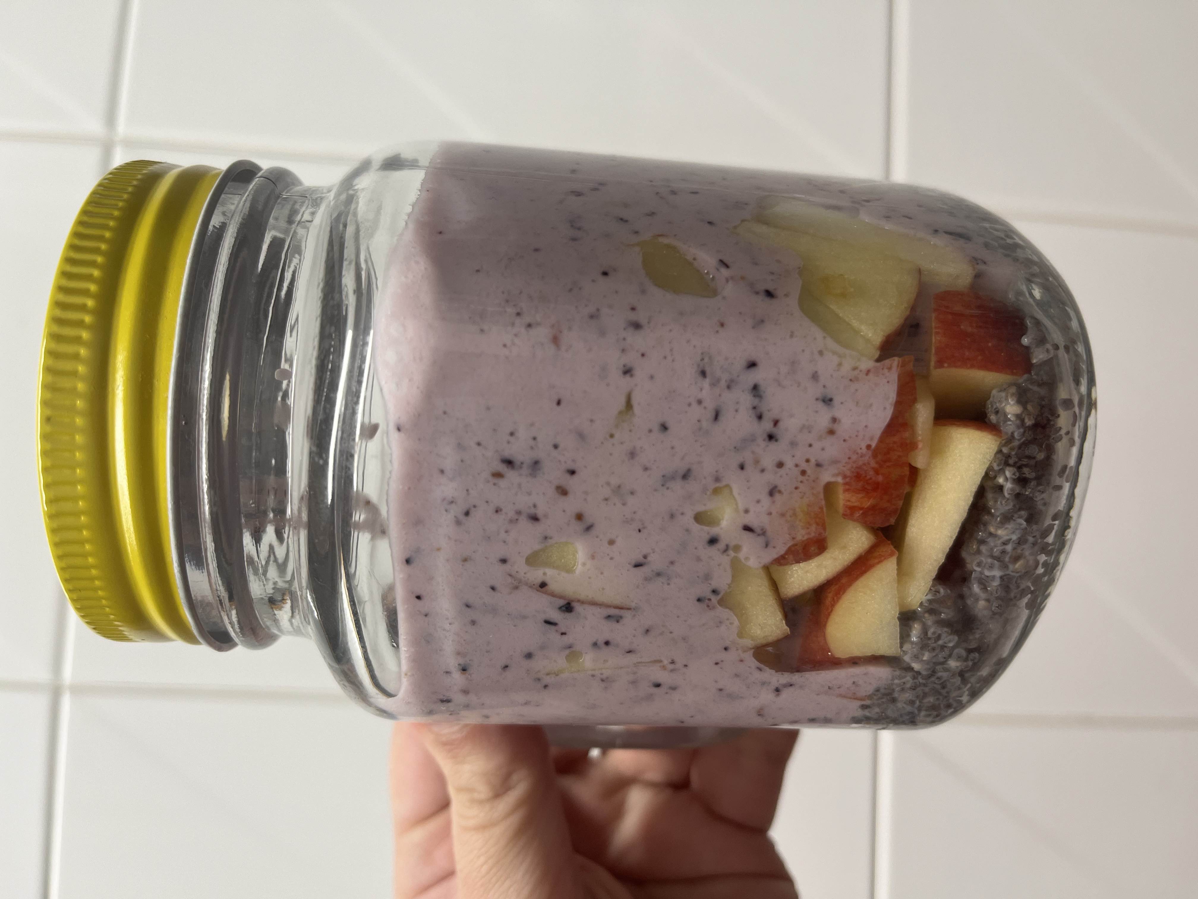 A layered jar containing chia seeds, apple slices, and blueberry yogurt, offering a nutritious and balanced snack.