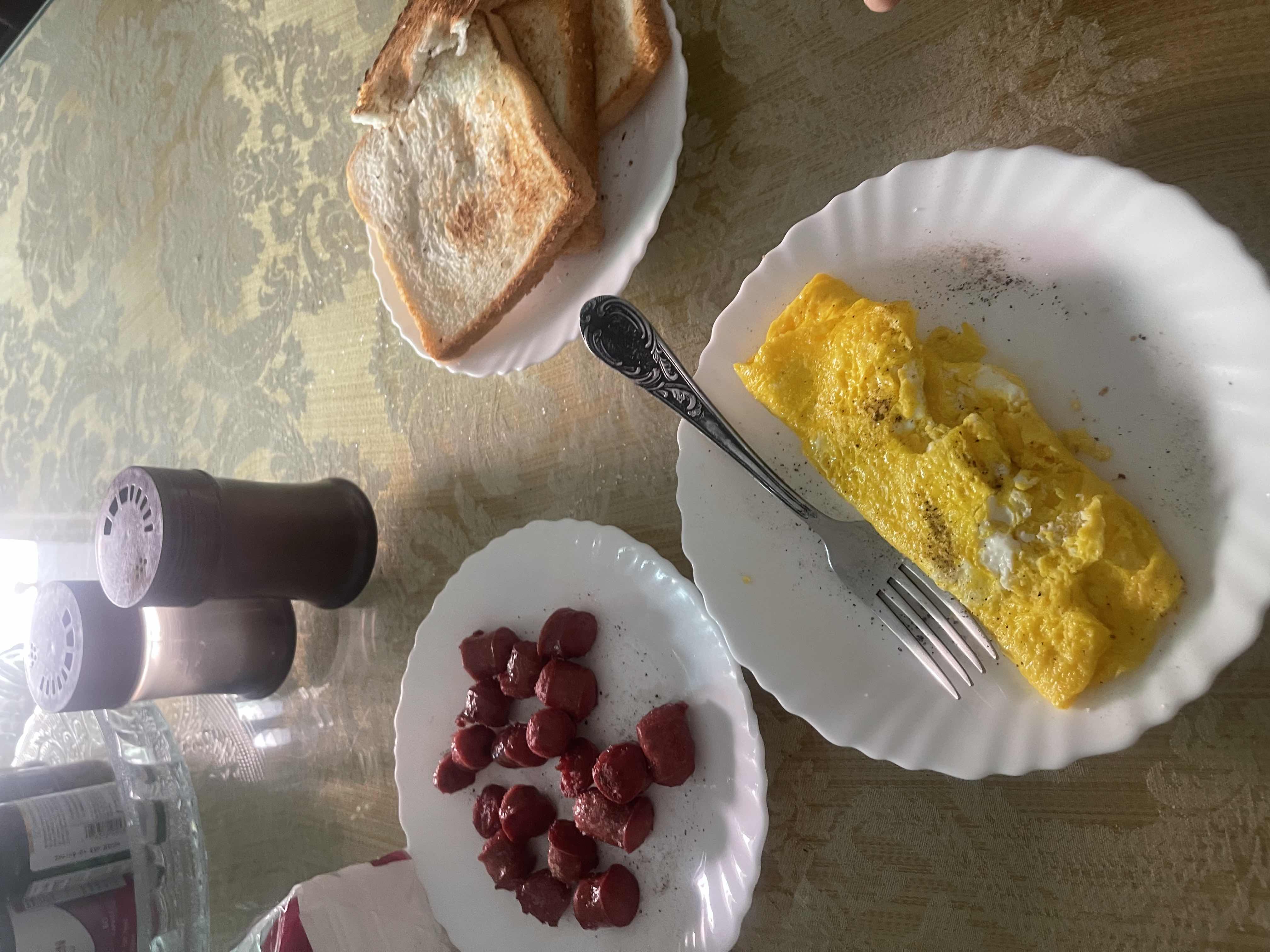 A meal consisting of a 2-egg omelette, 4 beef sausages, and 4 pieces of white bread, providing a balanced mix of protein, carbohydrates, and fats.