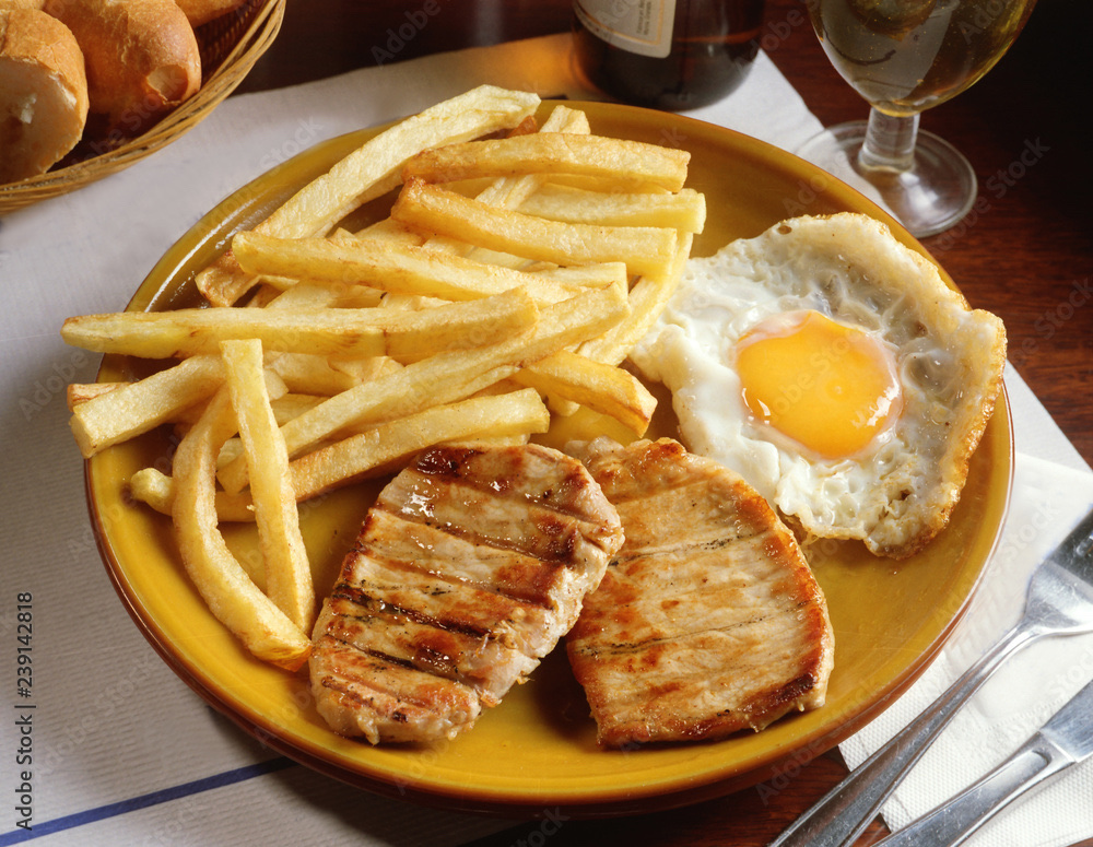 A meal consisting of French fries, grilled pork, and a fried egg, providing a balanced mix of protein, carbs, and fats.
