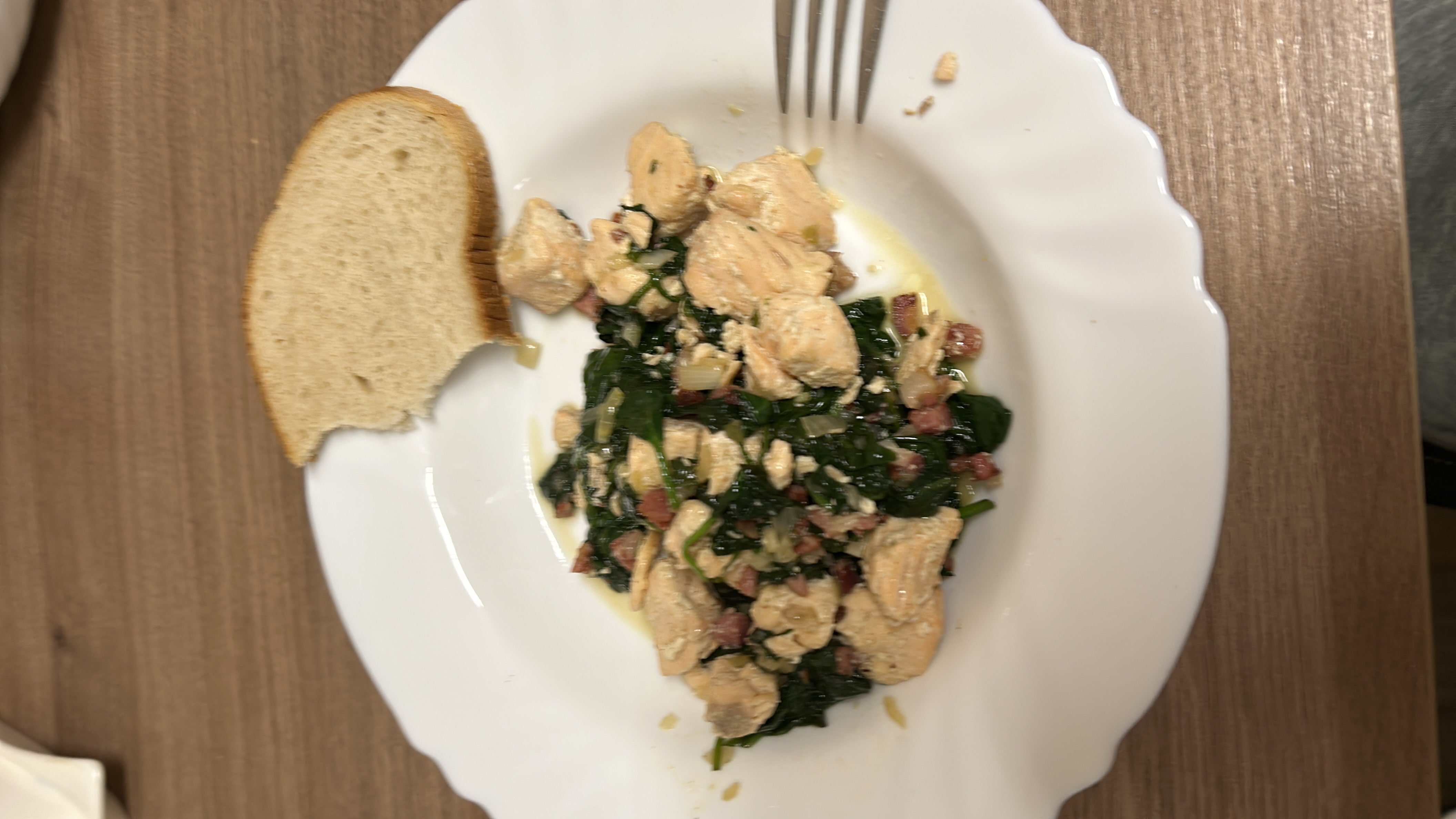 A dish consisting of sautéed chicken, spinach, bacon, and a slice of bread, providing a balanced mix of protein, carbs, and fats.