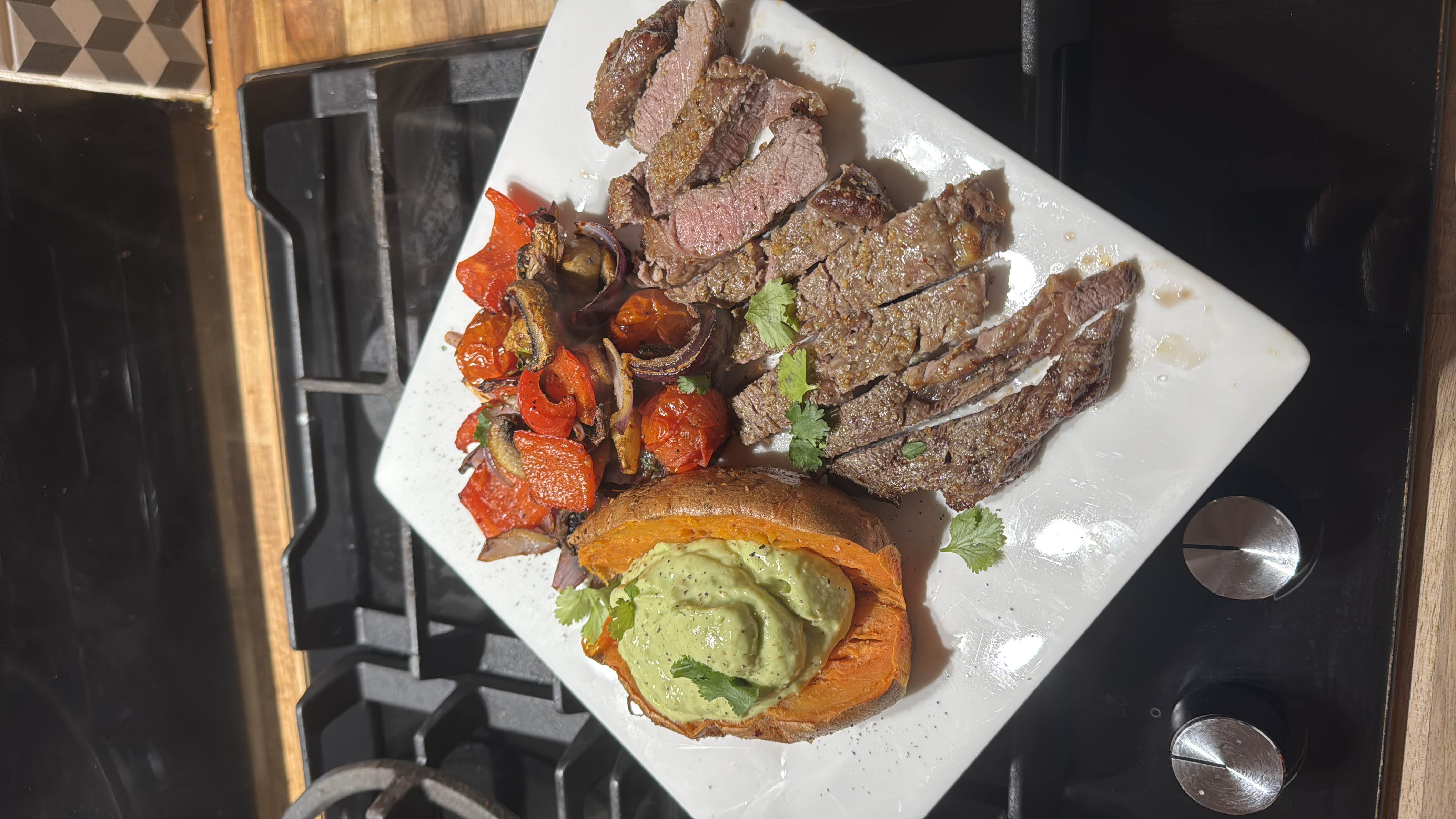 A balanced meal featuring steak, roasted vegetables, a baked sweet potato topped with avocado sauce, providing a mix of protein, carbs, and healthy fats.