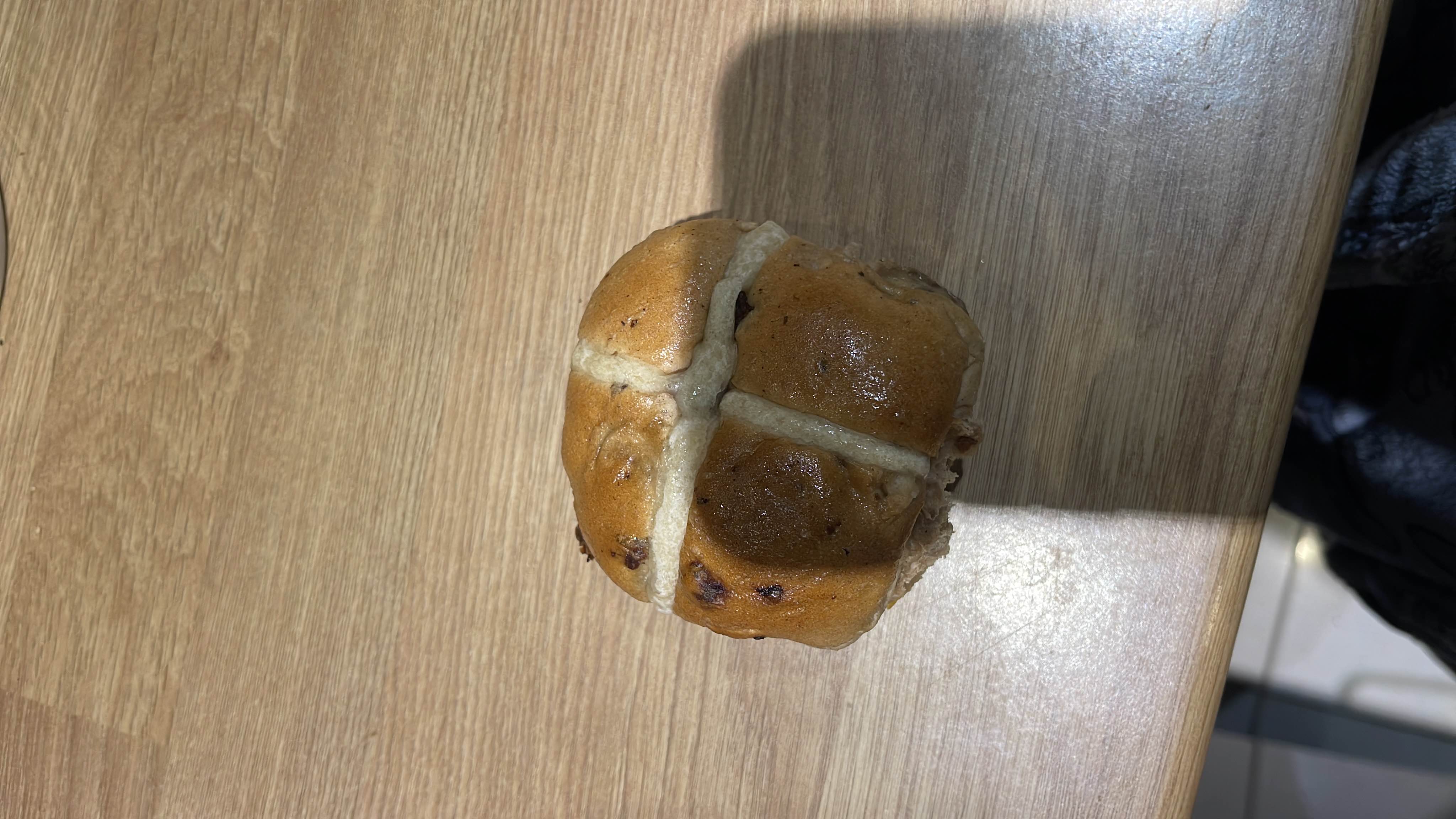 Half a hot cross bun, a sweet spiced bread with raisins, typically enjoyed as a snack or breakfast item.