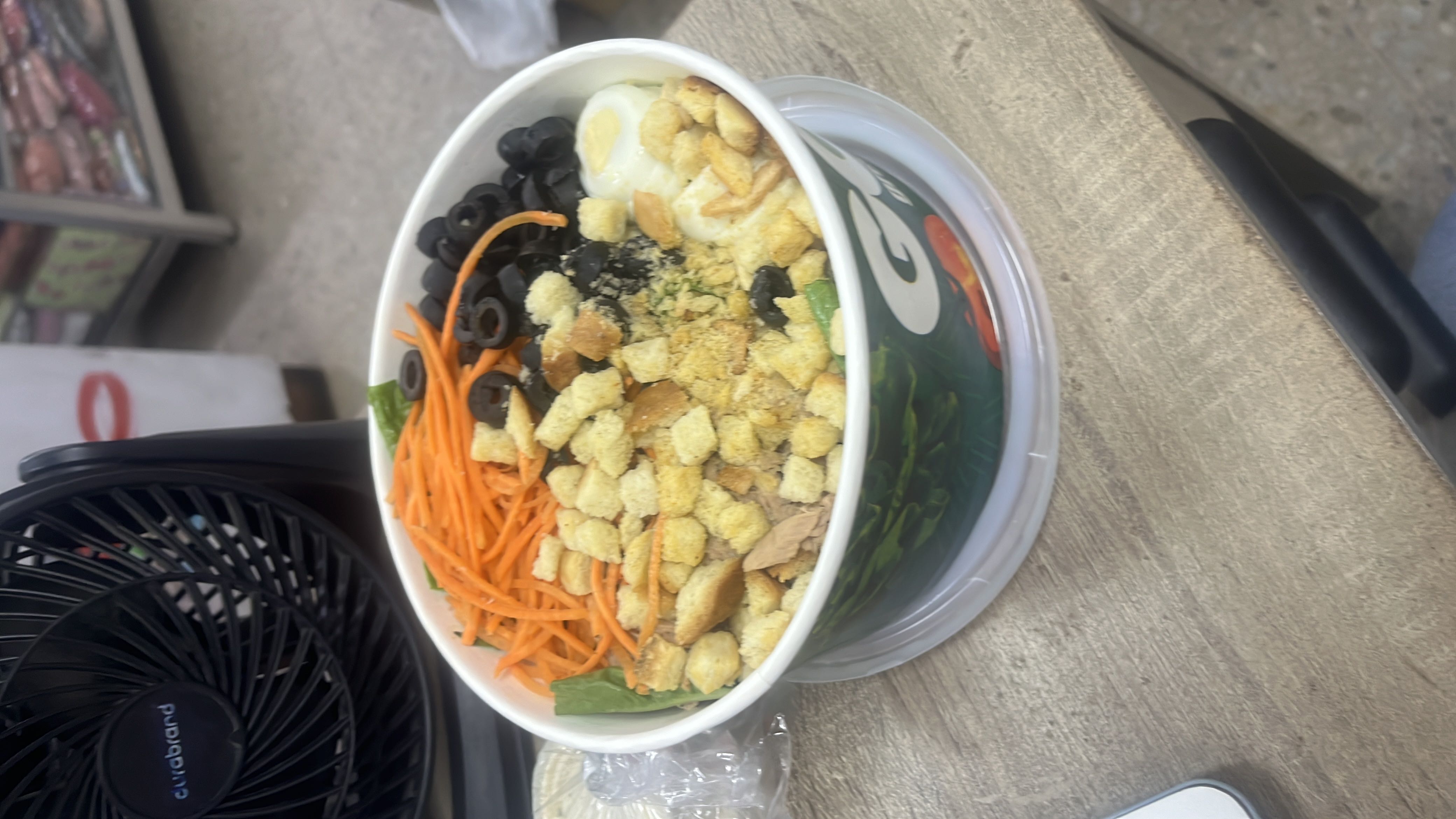 A healthy salad bowl containing croutons, carrots, black olives, boiled egg, and lettuce, offering a balanced mix of protein, carbs, and fats.