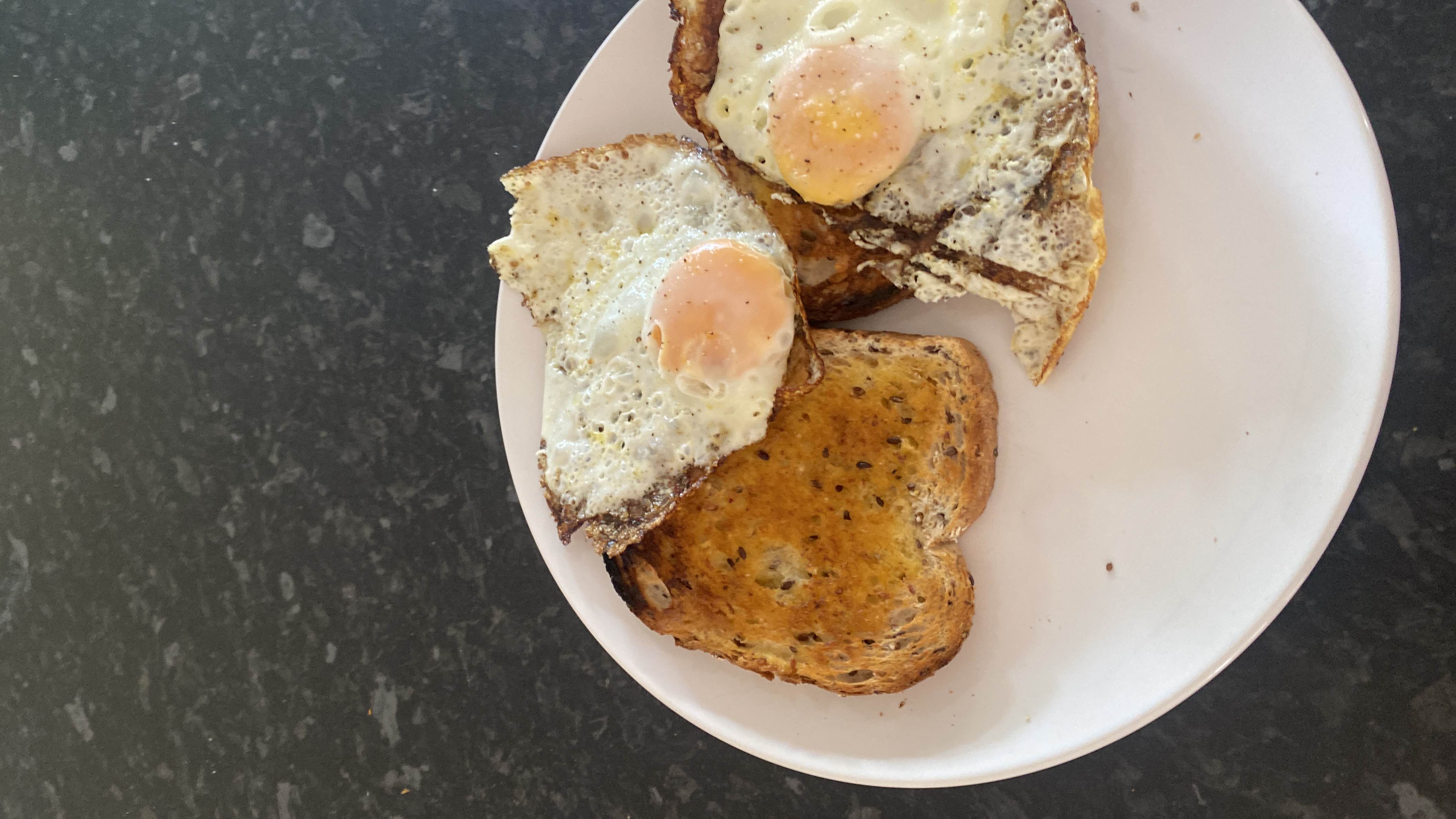 A simple breakfast consisting of two fried eggs and two slices of whole-grain toast, providing a balanced mix of protein, carbs, and fats.