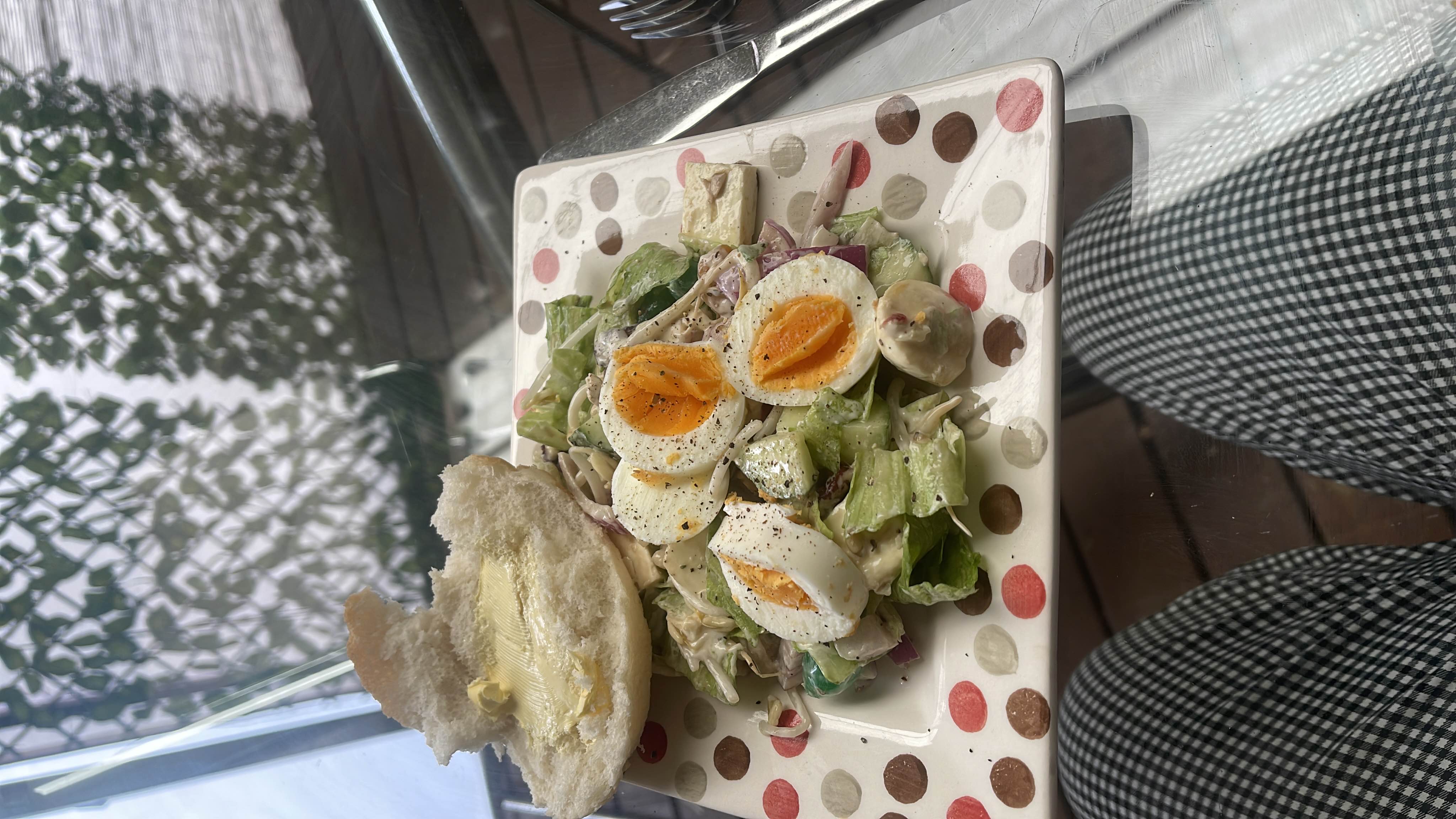 A fresh salad with boiled eggs, lettuce, cucumber, and mayonnaise, served with a buttered bread roll.