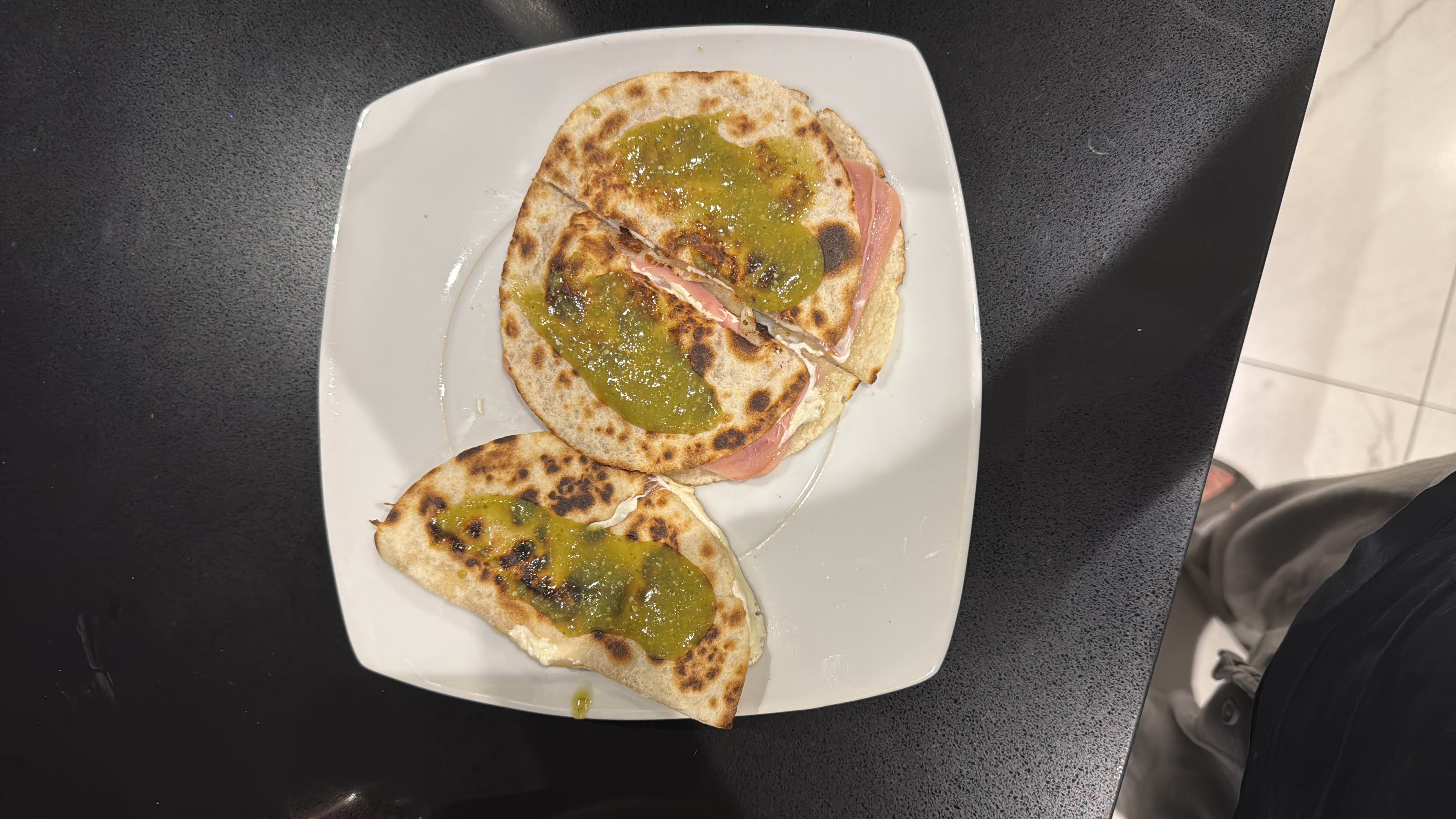 A dish consisting of tortillas filled with ham and cheese, topped with green sauce.