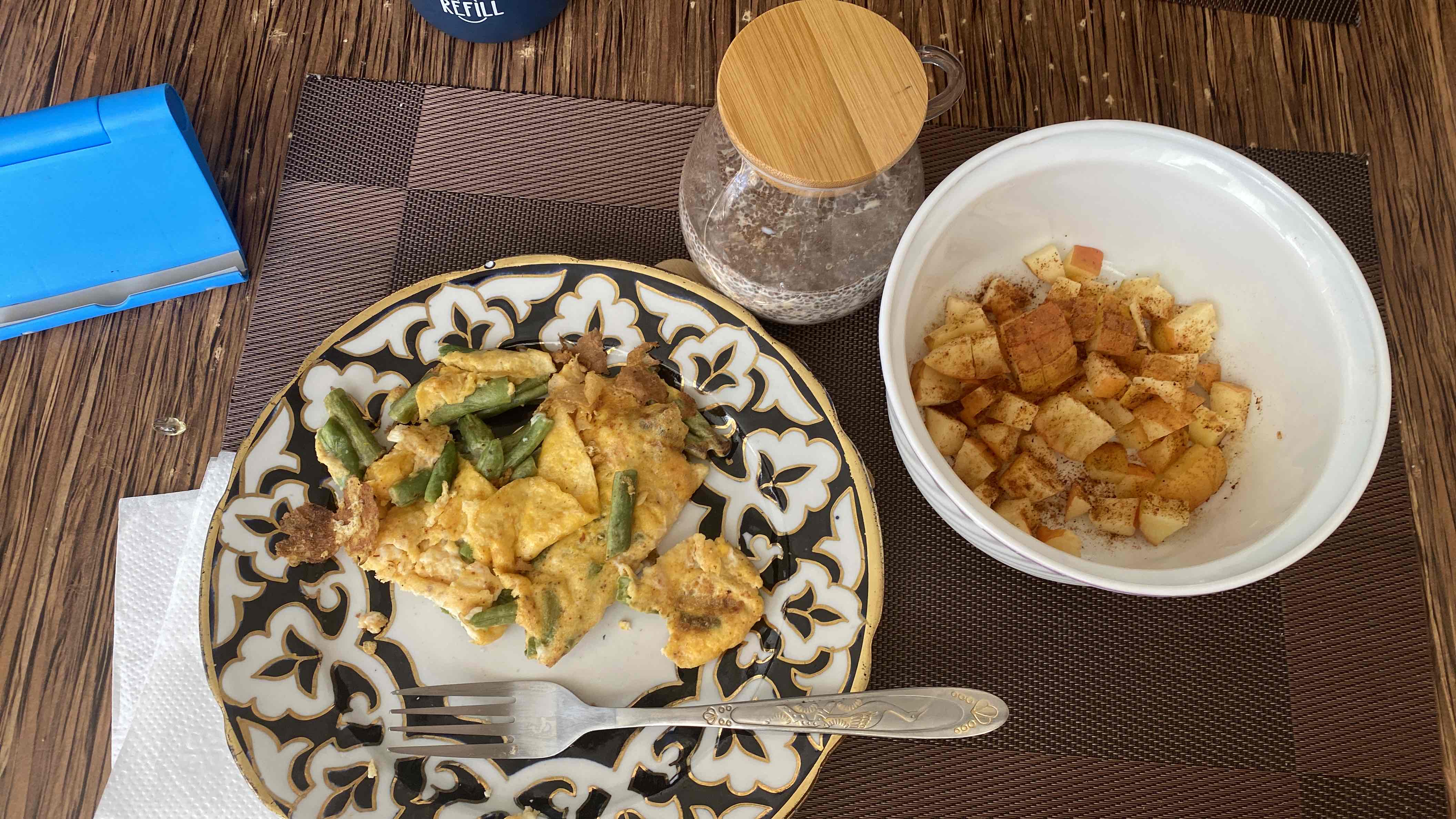 A meal consisting of an egg and green bean omelette, a bowl of diced apples with cinnamon, and a jar of chia seed pudding.