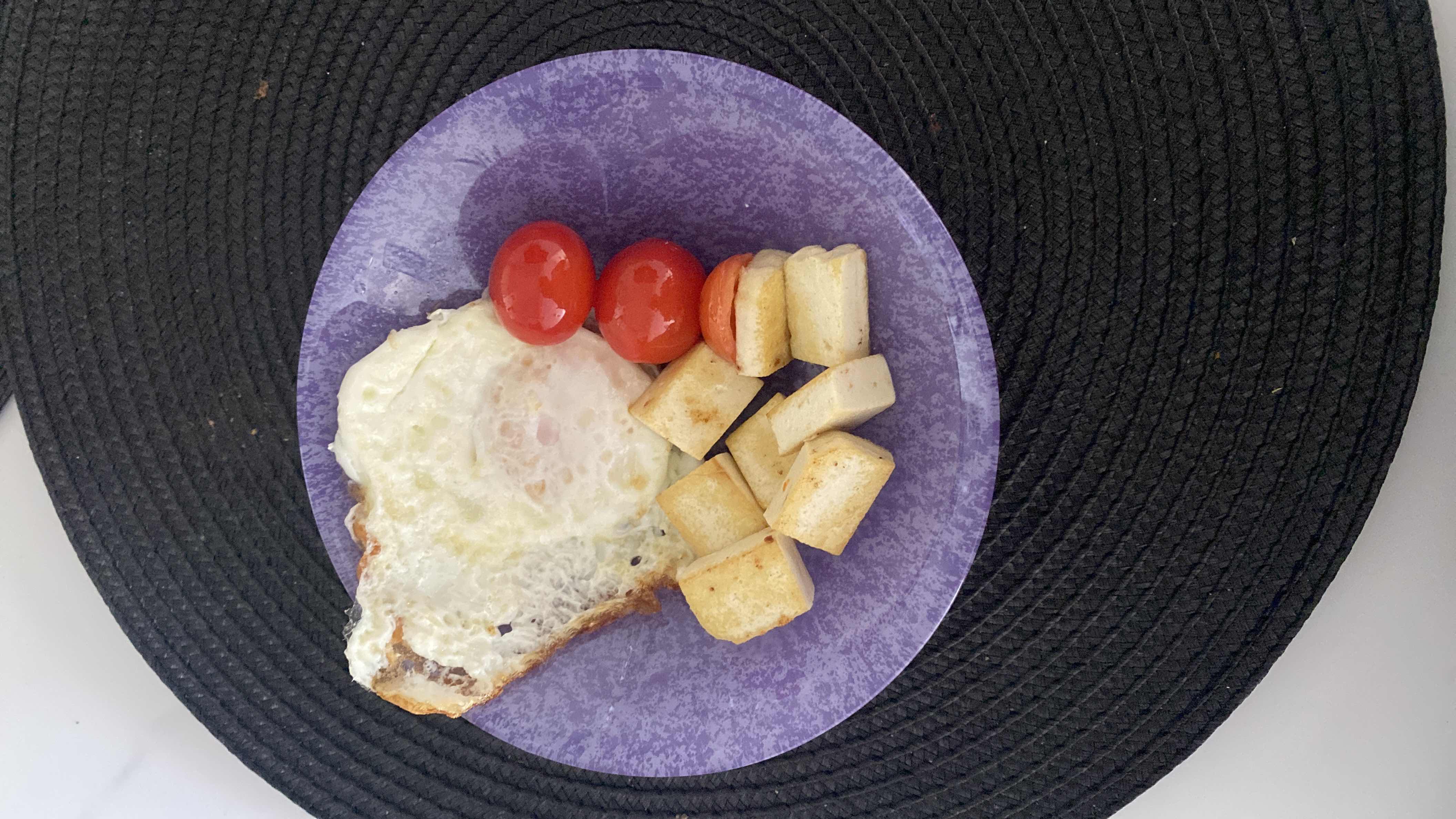 A balanced meal consisting of a fried egg, cherry tomatoes, and tofu cubes, providing a good mix of protein, fats, and carbs.