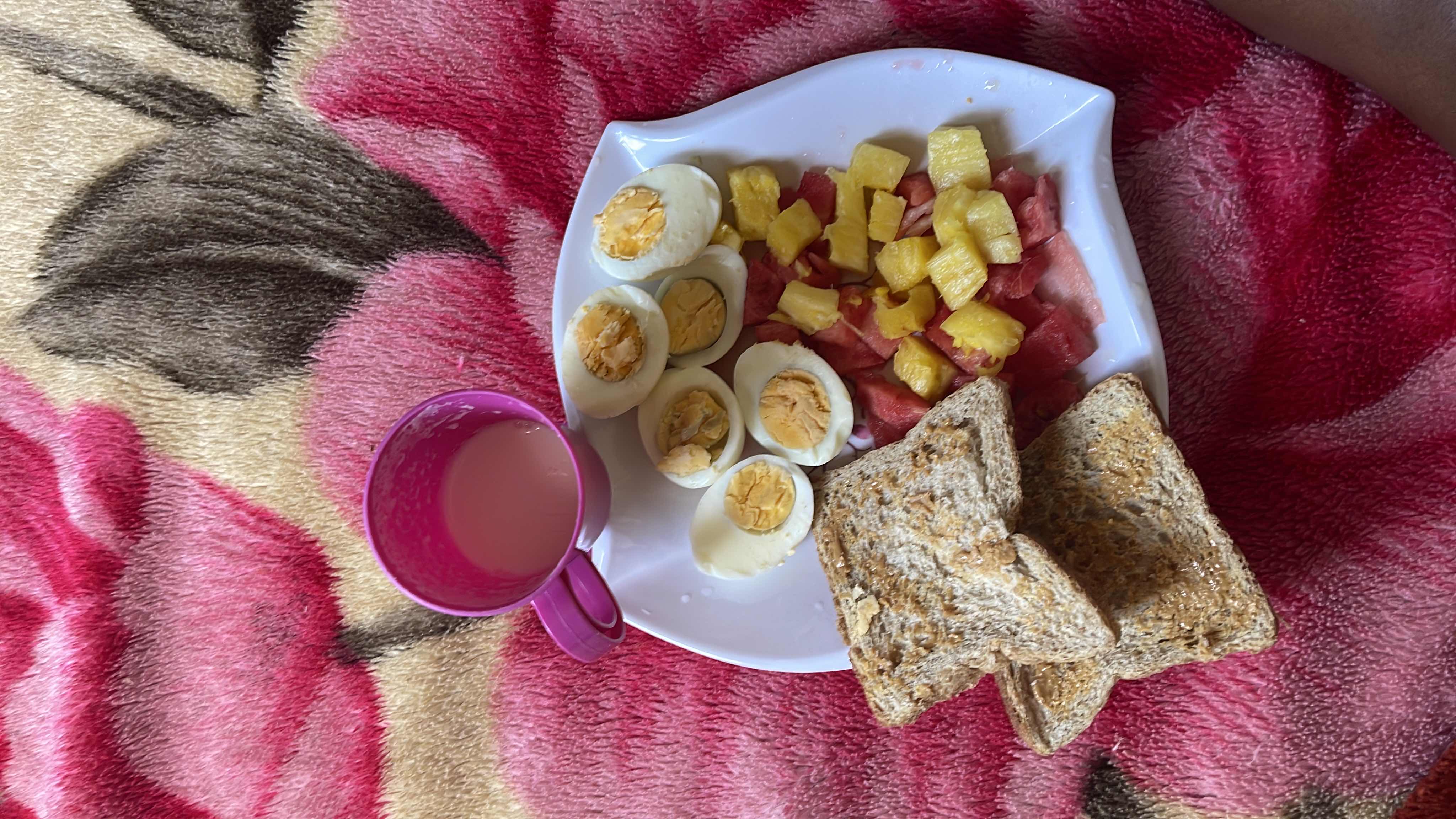 A balanced meal consisting of boiled eggs, fresh fruits (pineapple and watermelon), whole grain bread, and a cup of milk.
