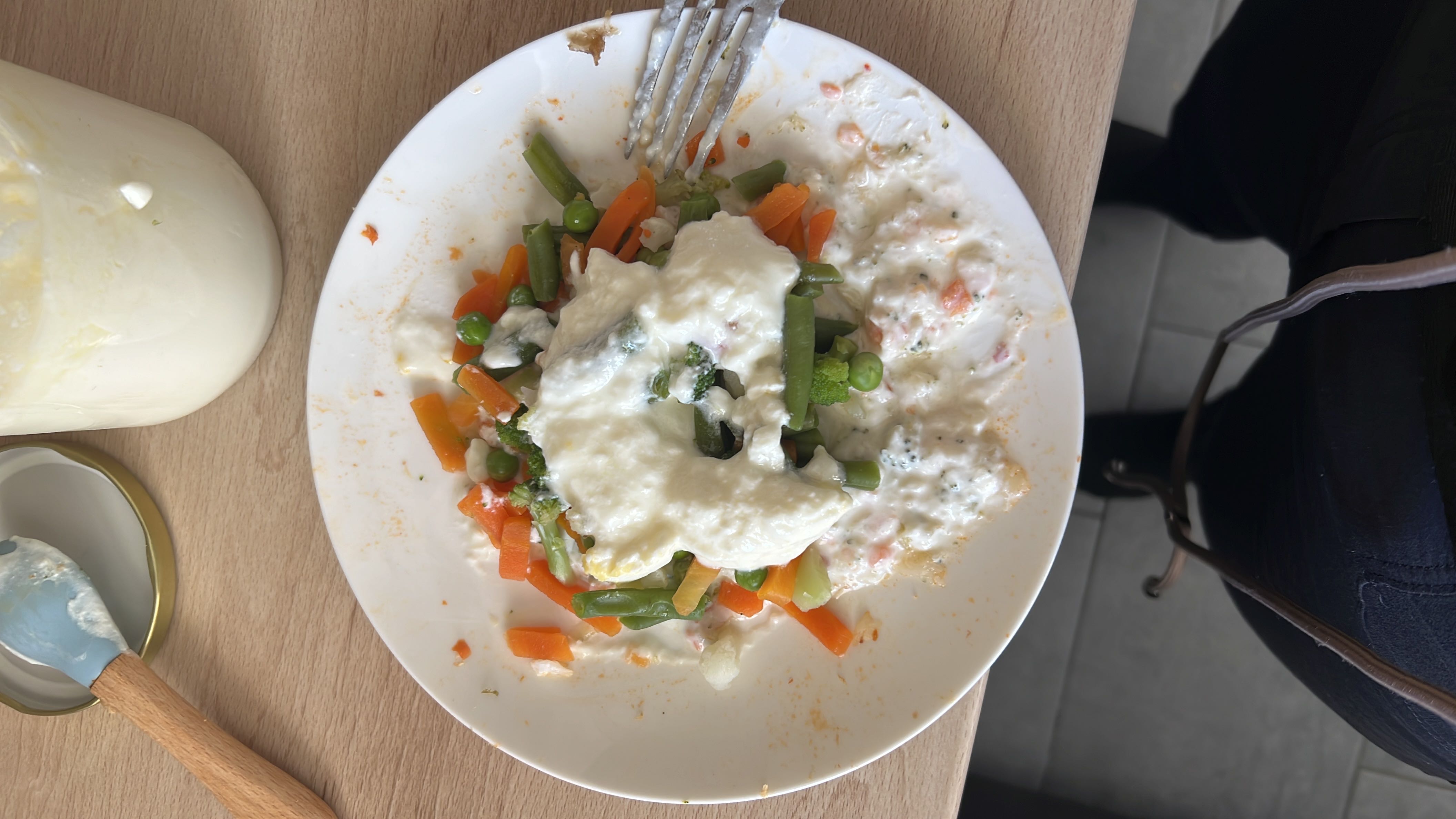 A healthy dish consisting of steamed vegetables like carrots, green beans, peas, and broccoli, topped with yogurt.