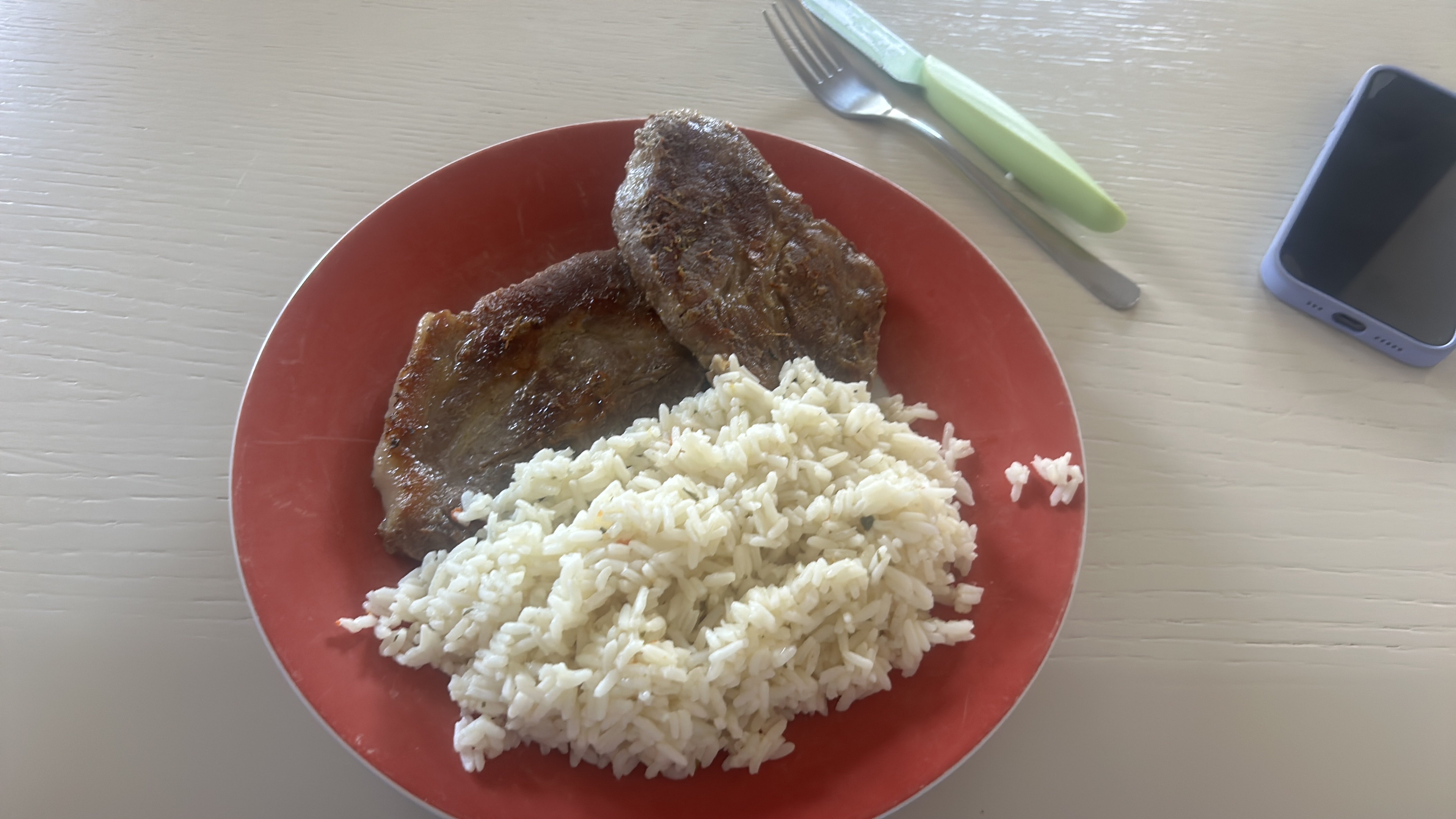 A plate containing cooked rice and two pieces of grilled steak, providing a balanced mix of protein, carbohydrates, and fats.