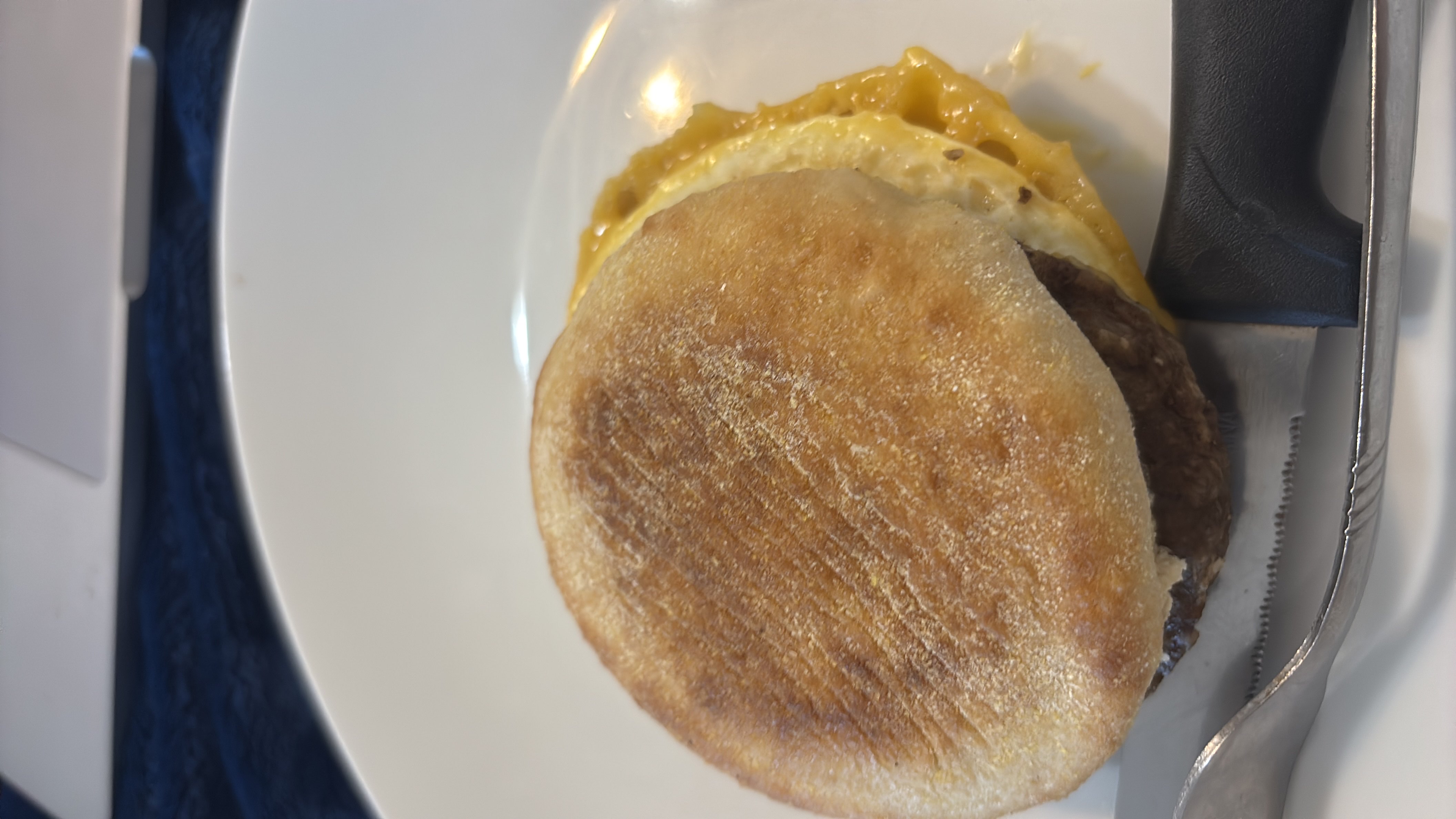 A breakfast sandwich consisting of an English muffin, egg, cheese, and sausage patty.
