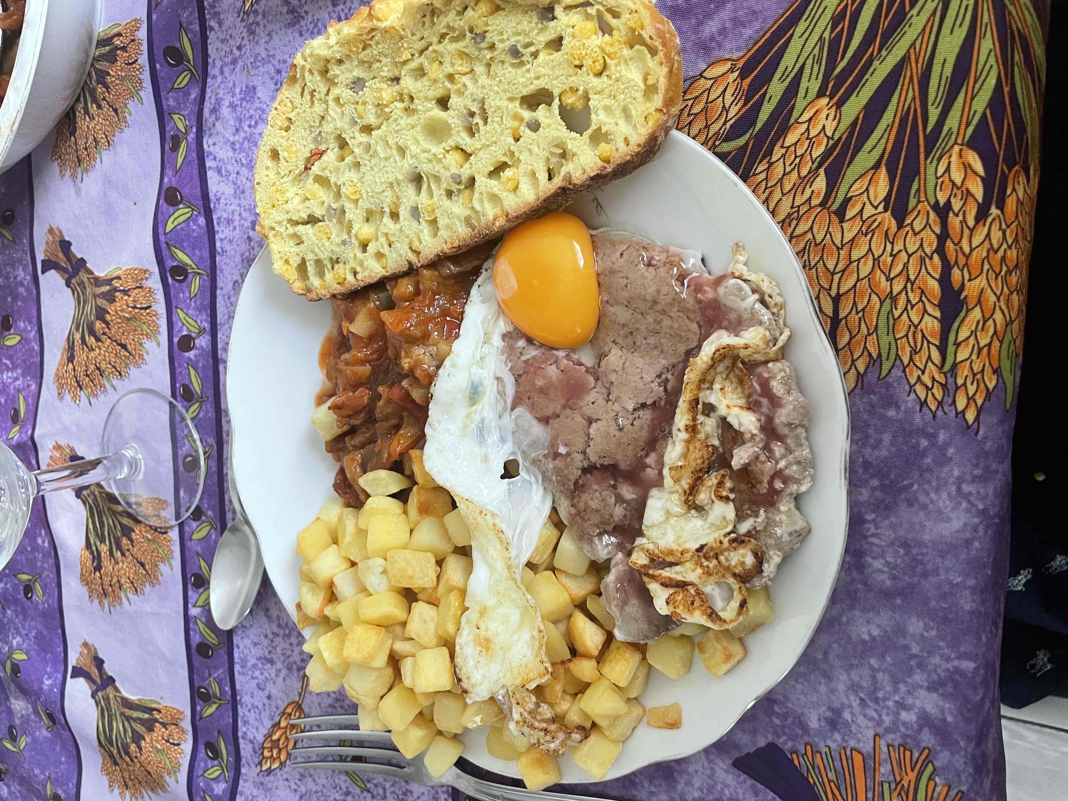 A hearty meal consisting of fried potatoes, a fried egg, a slice of bread, meat with sauce, and a vegetable stew.