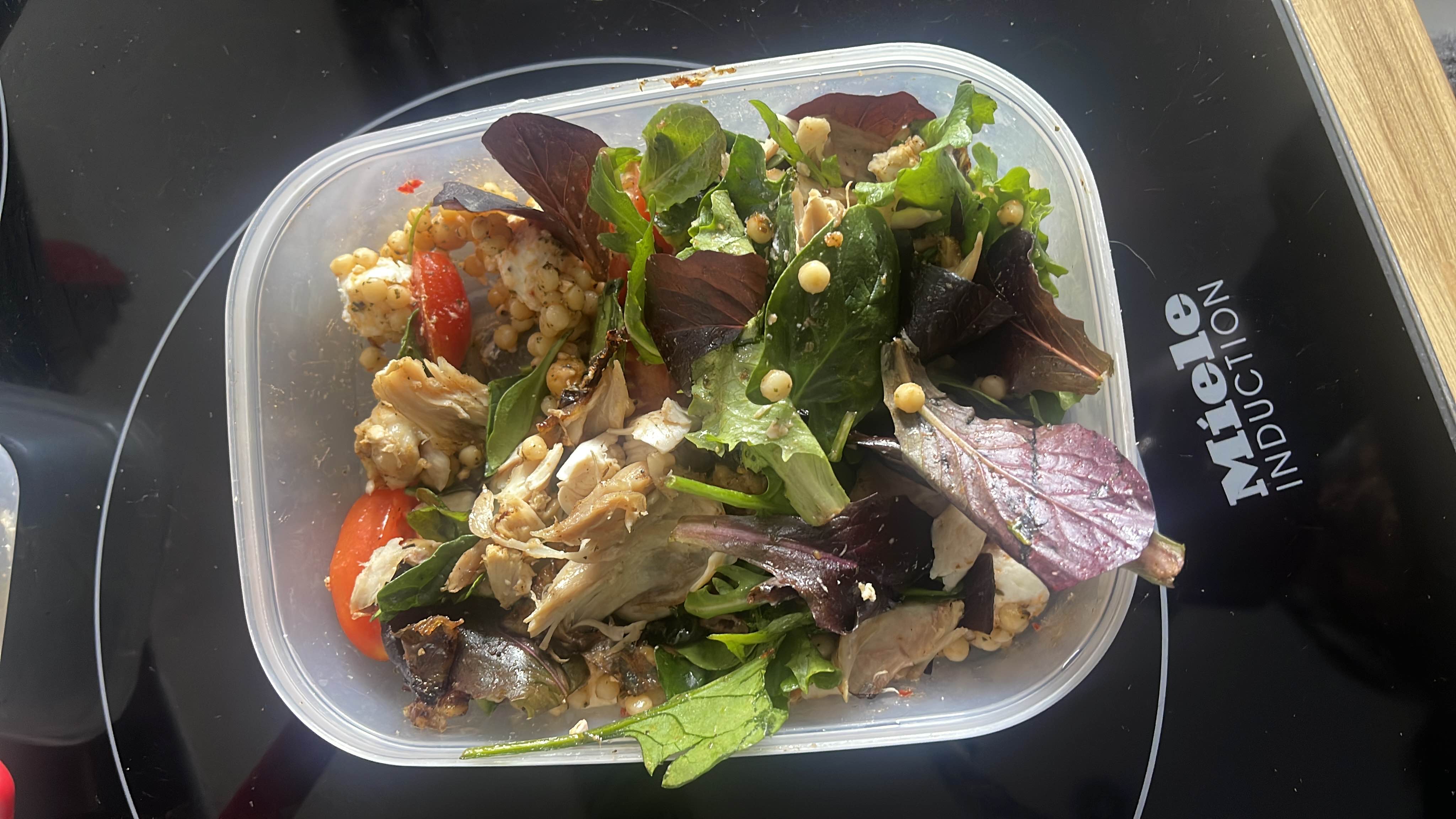 A healthy salad containing chicken, mixed greens, couscous, tomatoes, and a light dressing.