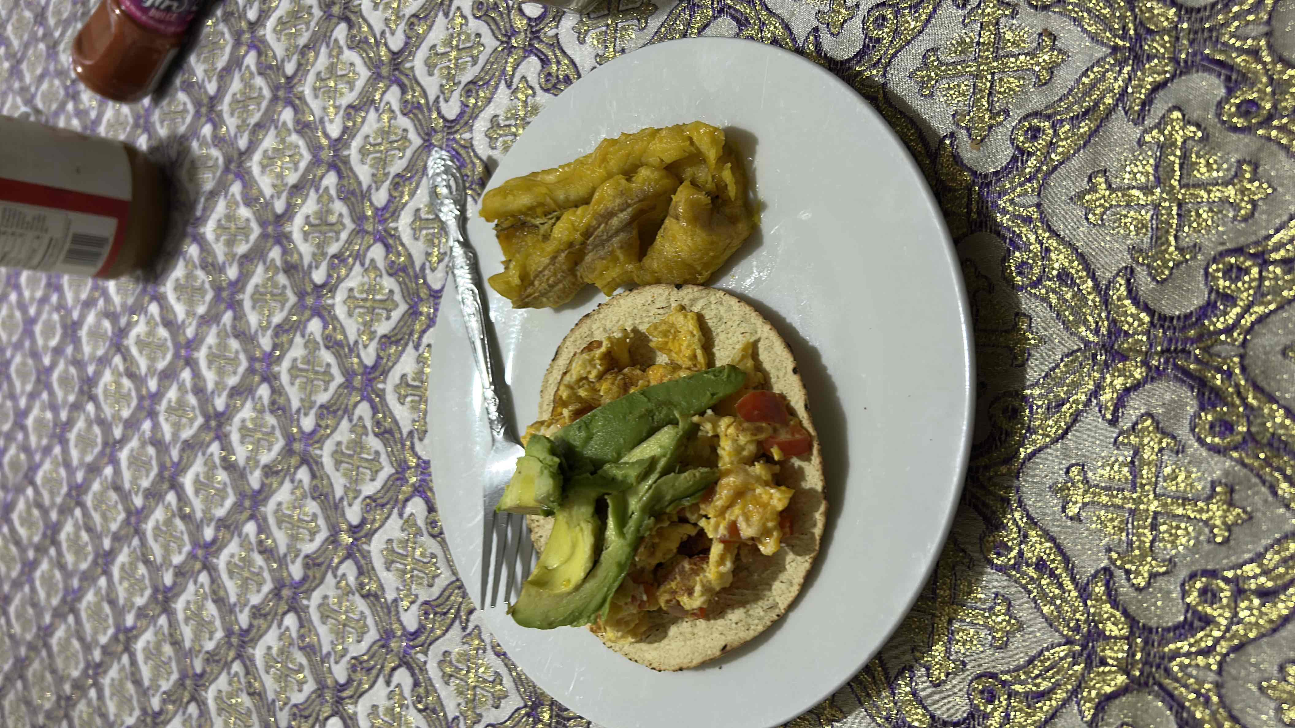 A balanced meal consisting of a tortilla topped with scrambled eggs, avocado slices, and a side of cooked plantains.