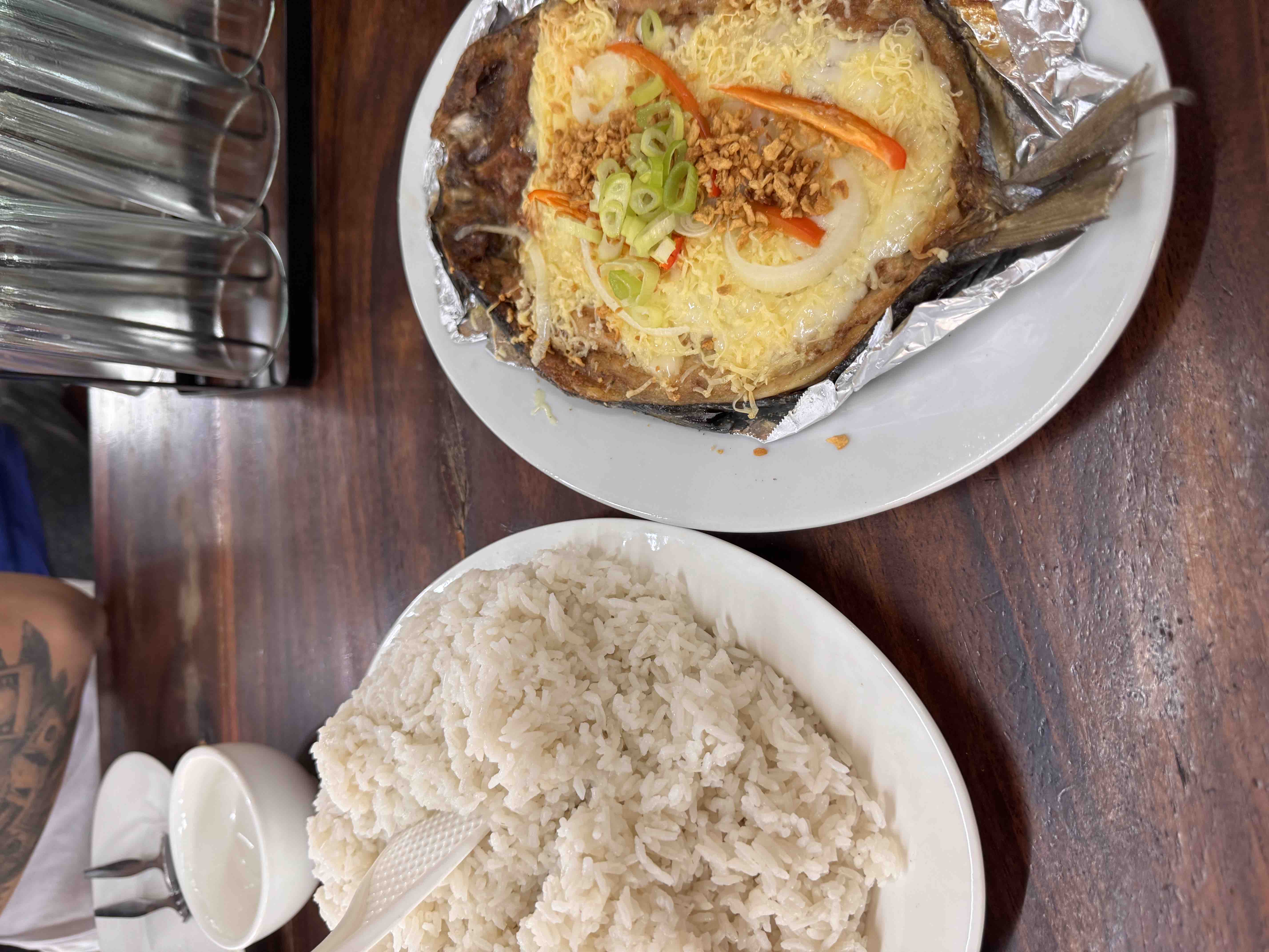 A meal consisting of steamed rice and grilled fish topped with cheese, onions, garlic, and peppers, providing a balanced mix of protein, carbs, and fats.