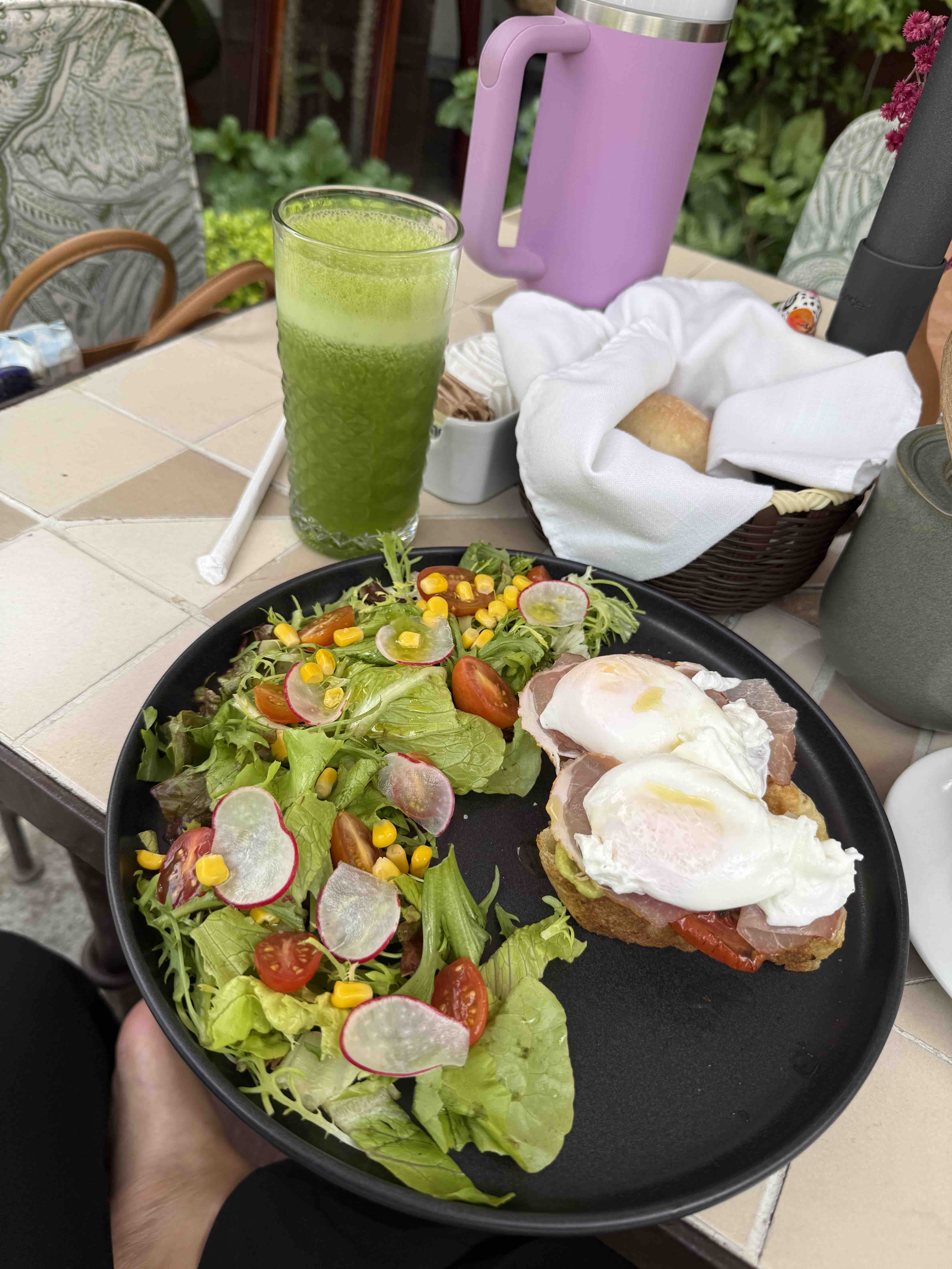 A healthy meal consisting of a fresh salad with lettuce, radish, cherry tomatoes, and corn, served with poached eggs on bread and accompanied by a green juice.