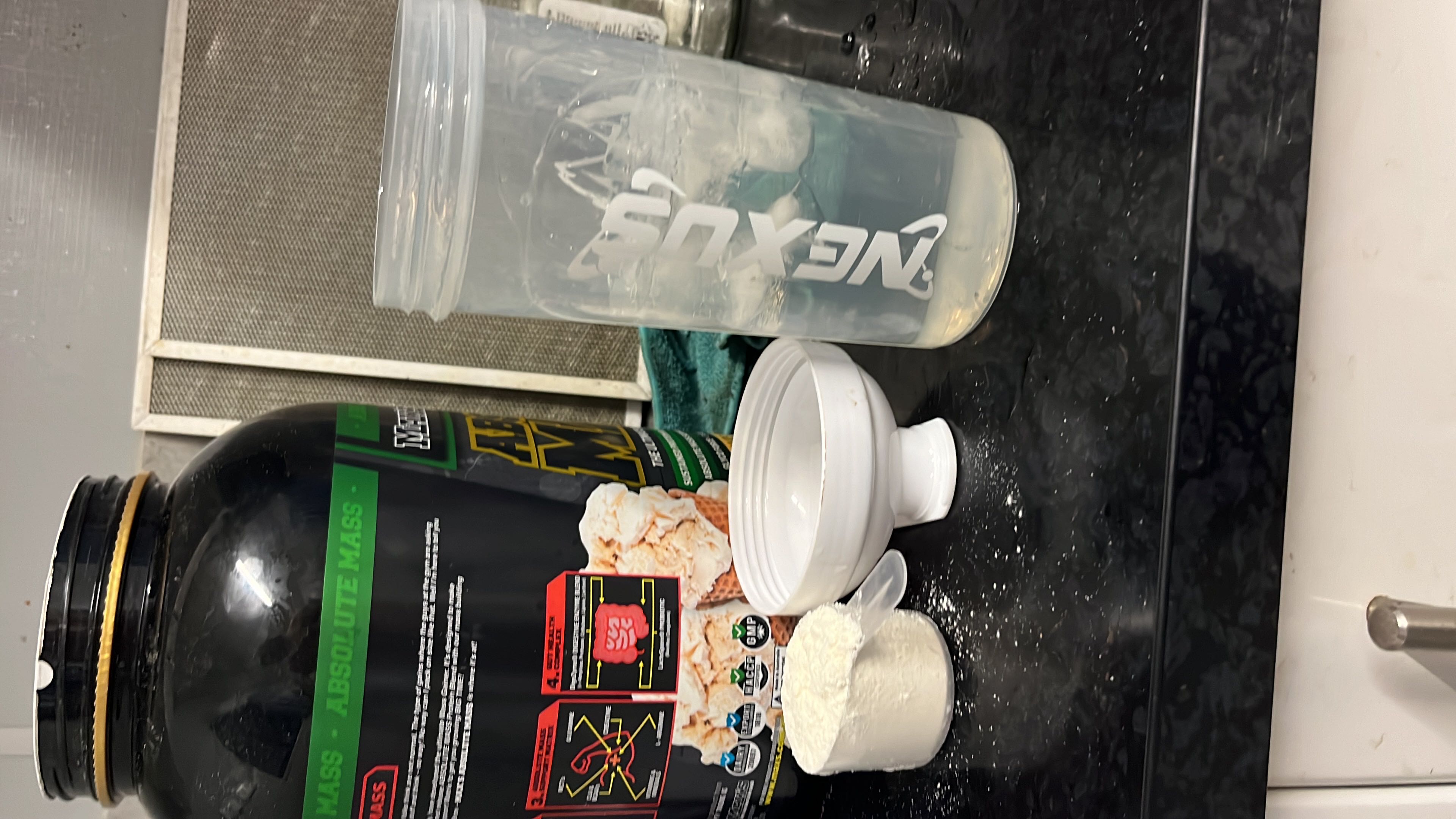 The image shows a protein supplement labeled 'Absolute Mass' with a scoop of powder and a shaker bottle, indicating a high-calorie, high-carb, and high-protein nutritional profile.
