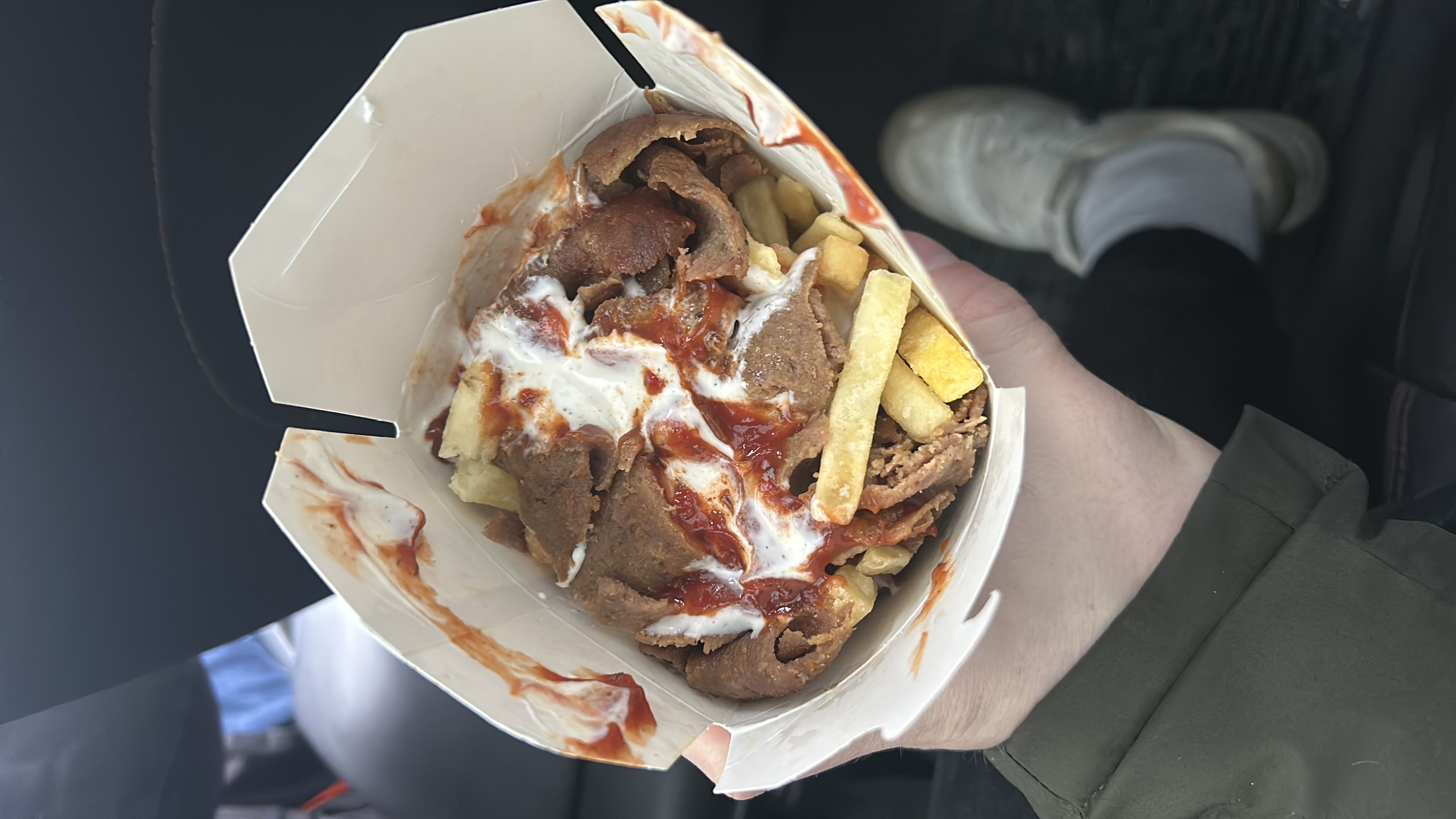 A fast-food dish consisting of fries, doner meat, and sauces, served in a takeaway box.