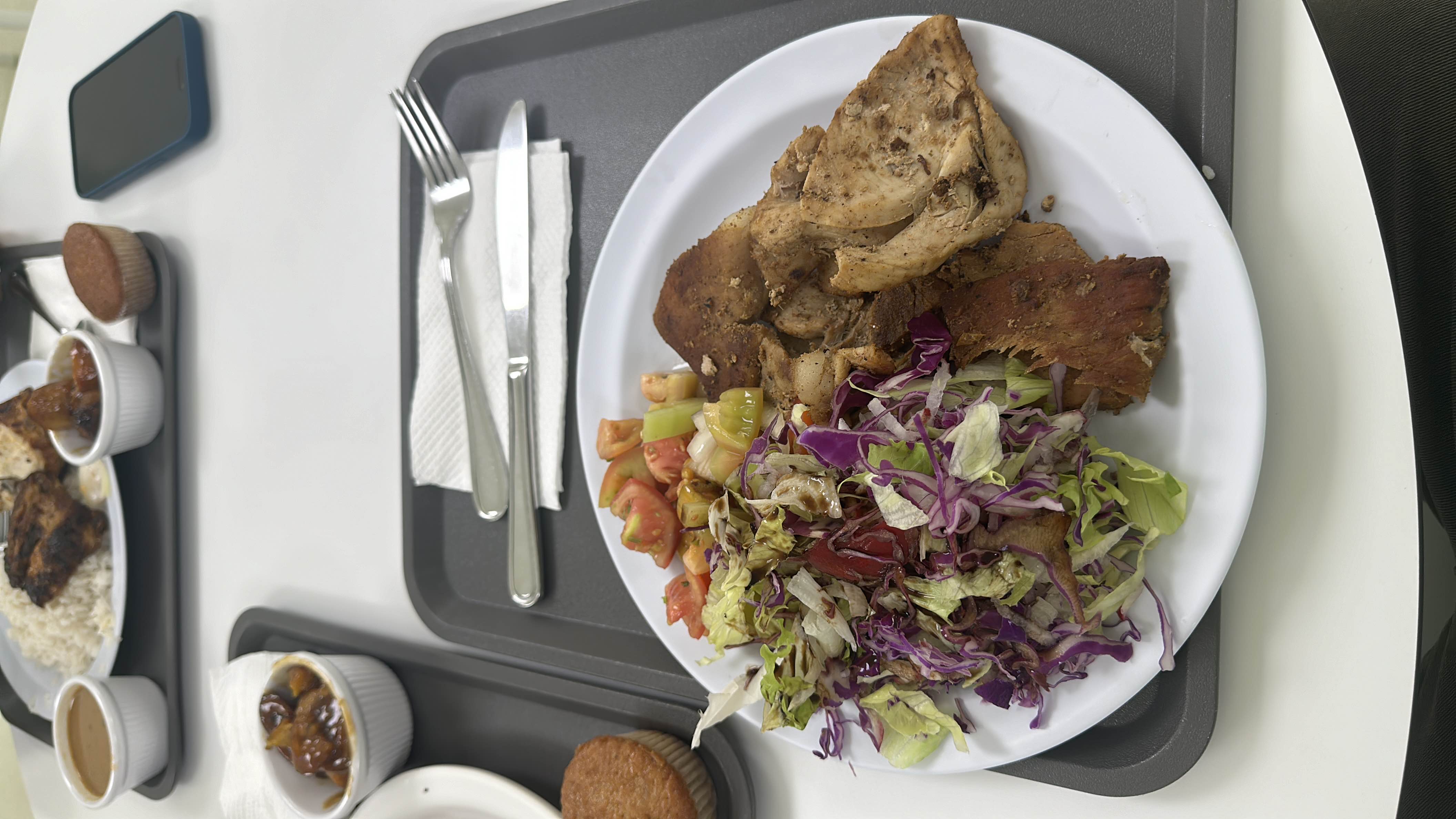 A balanced meal consisting of grilled chicken, fresh salad, tomatoes, cucumbers, a bread slice, and a muffin.