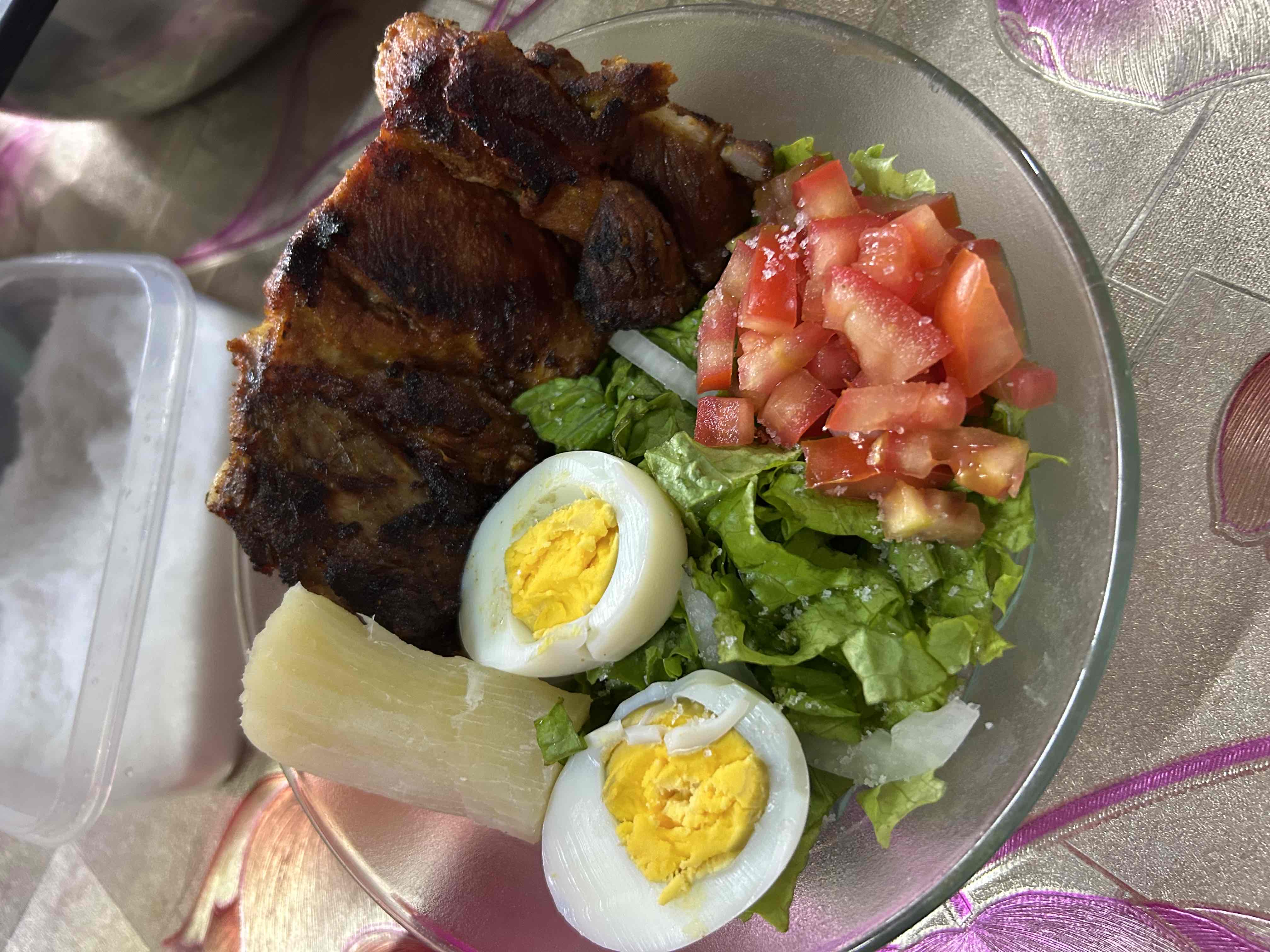 A balanced meal consisting of grilled meat, boiled egg, cassava, lettuce, and tomato, providing a good mix of protein, carbs, and fats.
