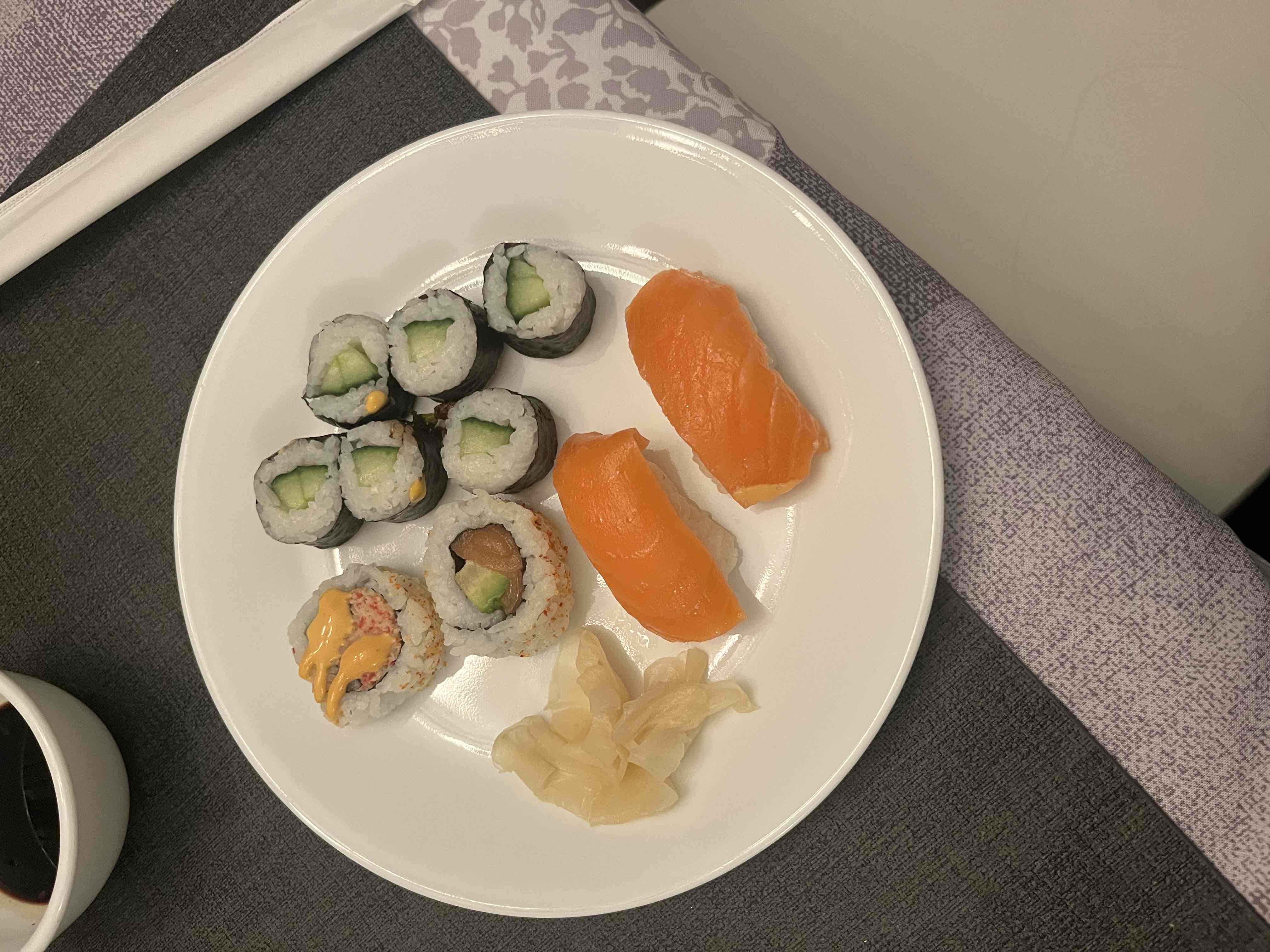 A plate of sushi including salmon nigiri, cucumber rolls, and crab rolls with ginger on the side.