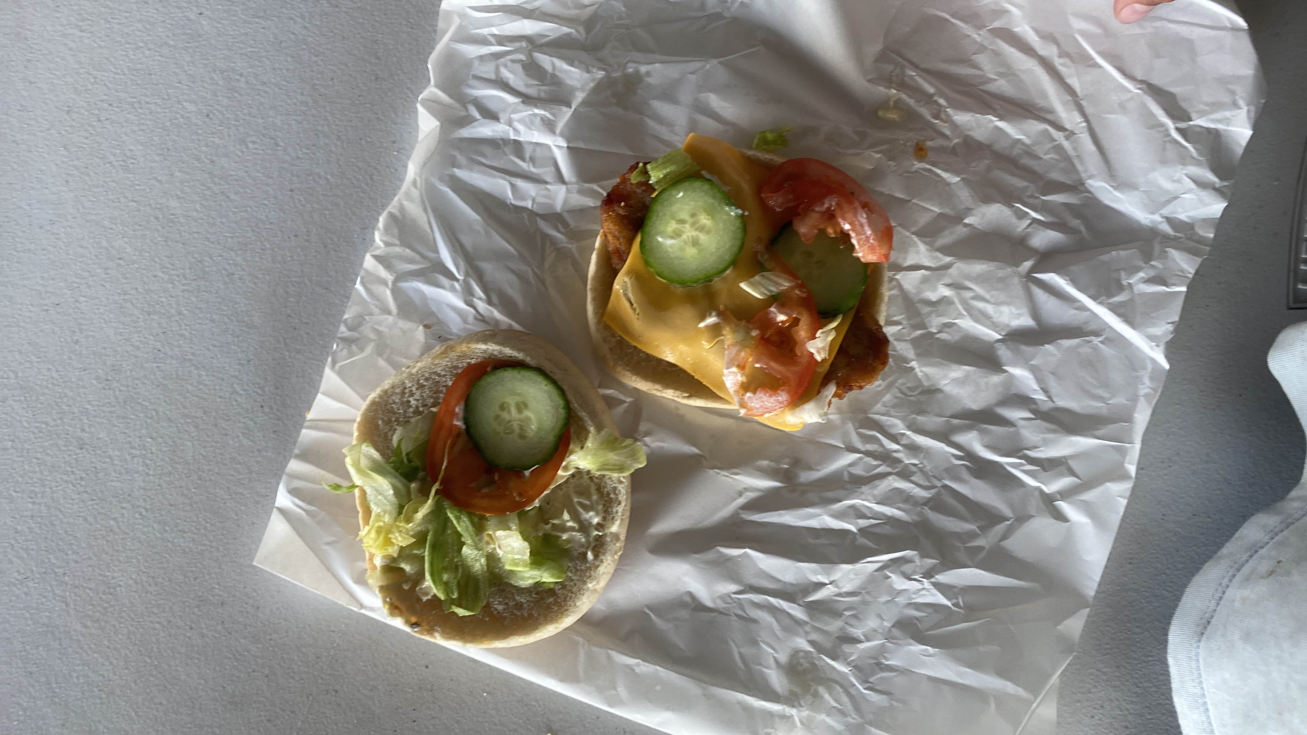 A sandwich with a fried chicken patty, cheese, lettuce, tomato, cucumber, and a bread bun.