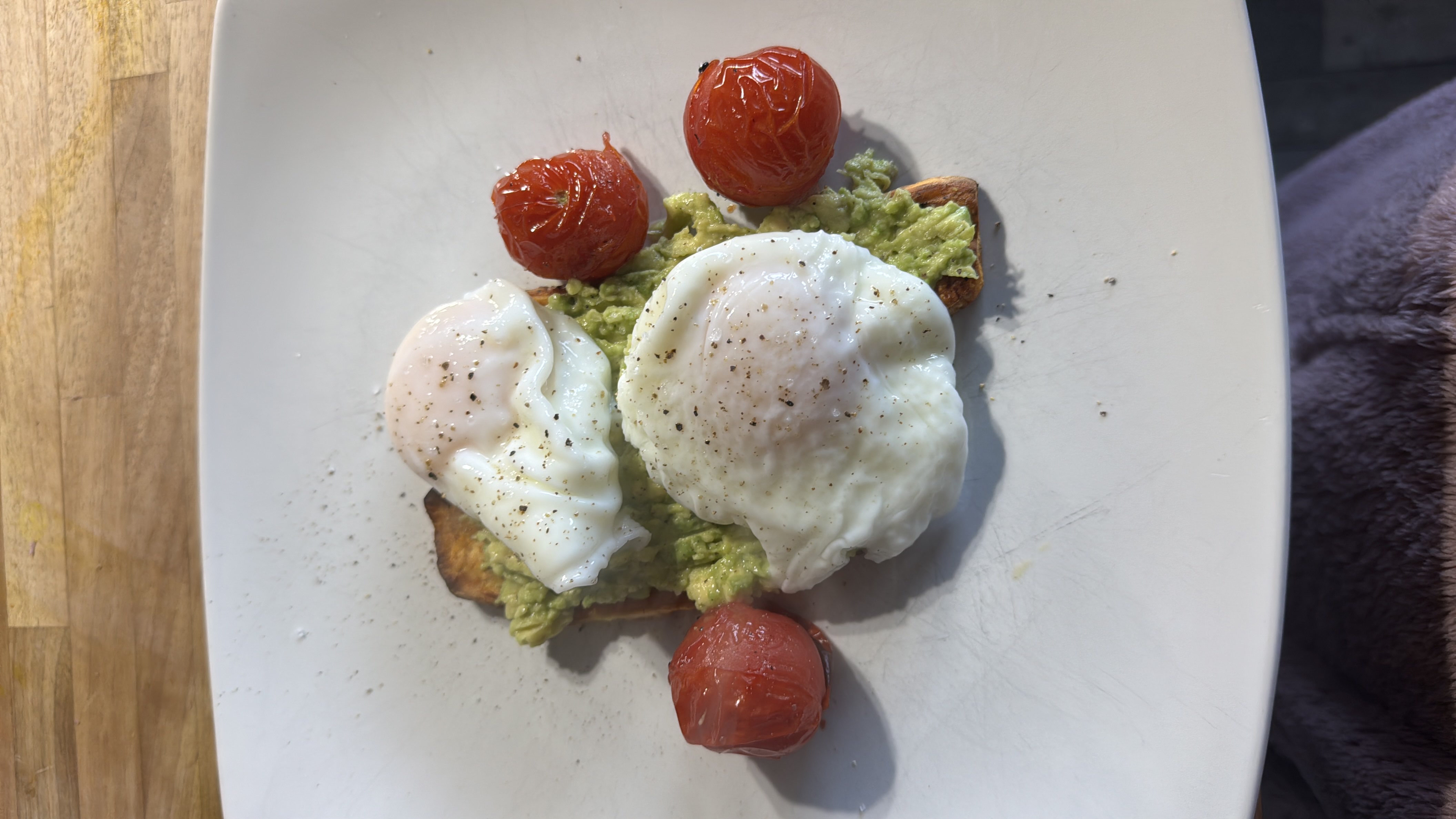 A healthy dish consisting of avocado and cherry tomatoes, topped with poached eggs and served with roasted sweet potato.