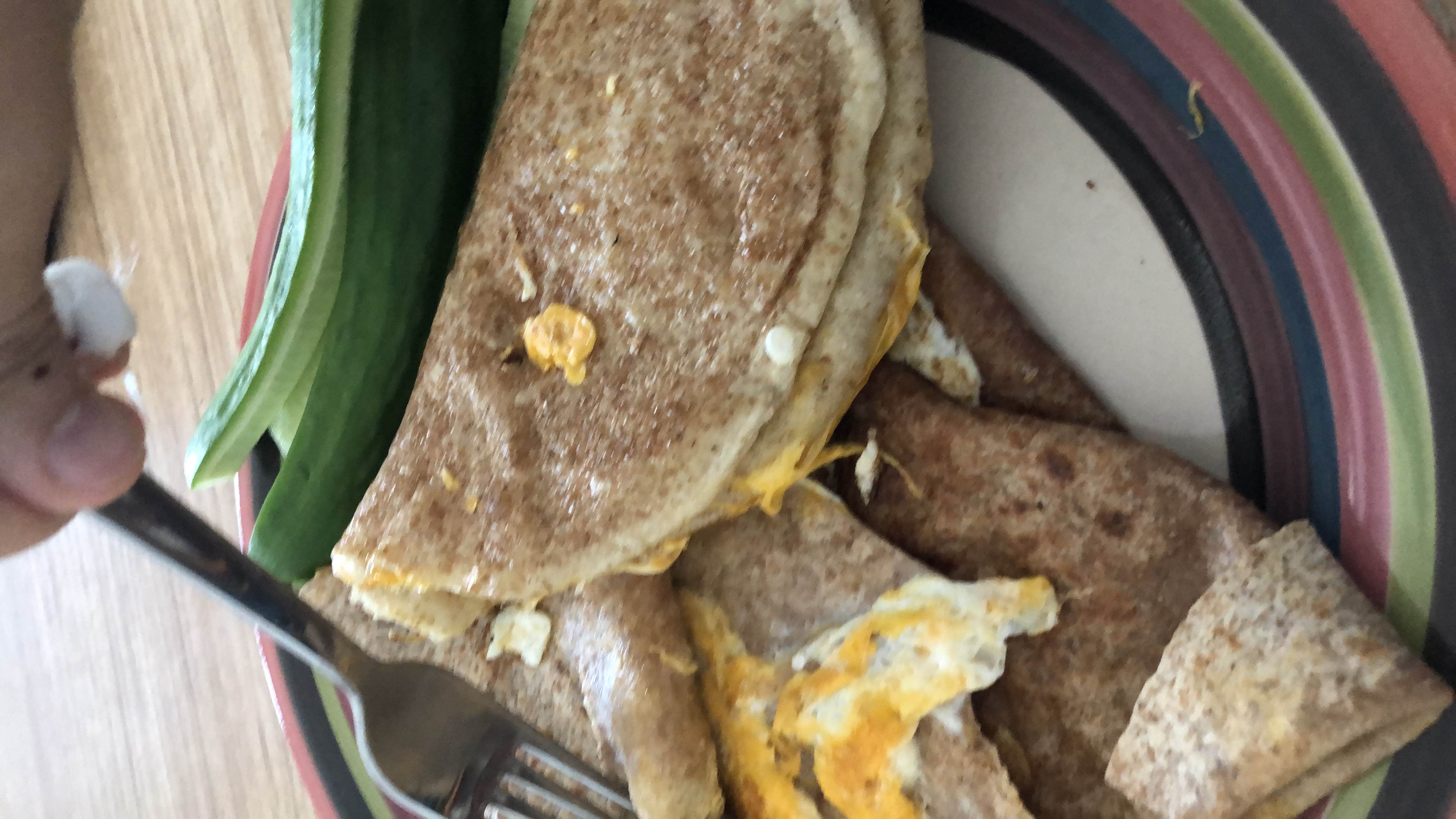 A plate containing whole wheat tortillas filled with eggs and cheese, served with fresh cucumber slices.