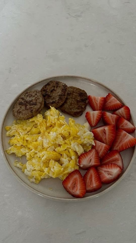A balanced plate consisting of scrambled eggs, sausage patties, and fresh strawberries, providing a mix of protein, fats, and carbohydrates.