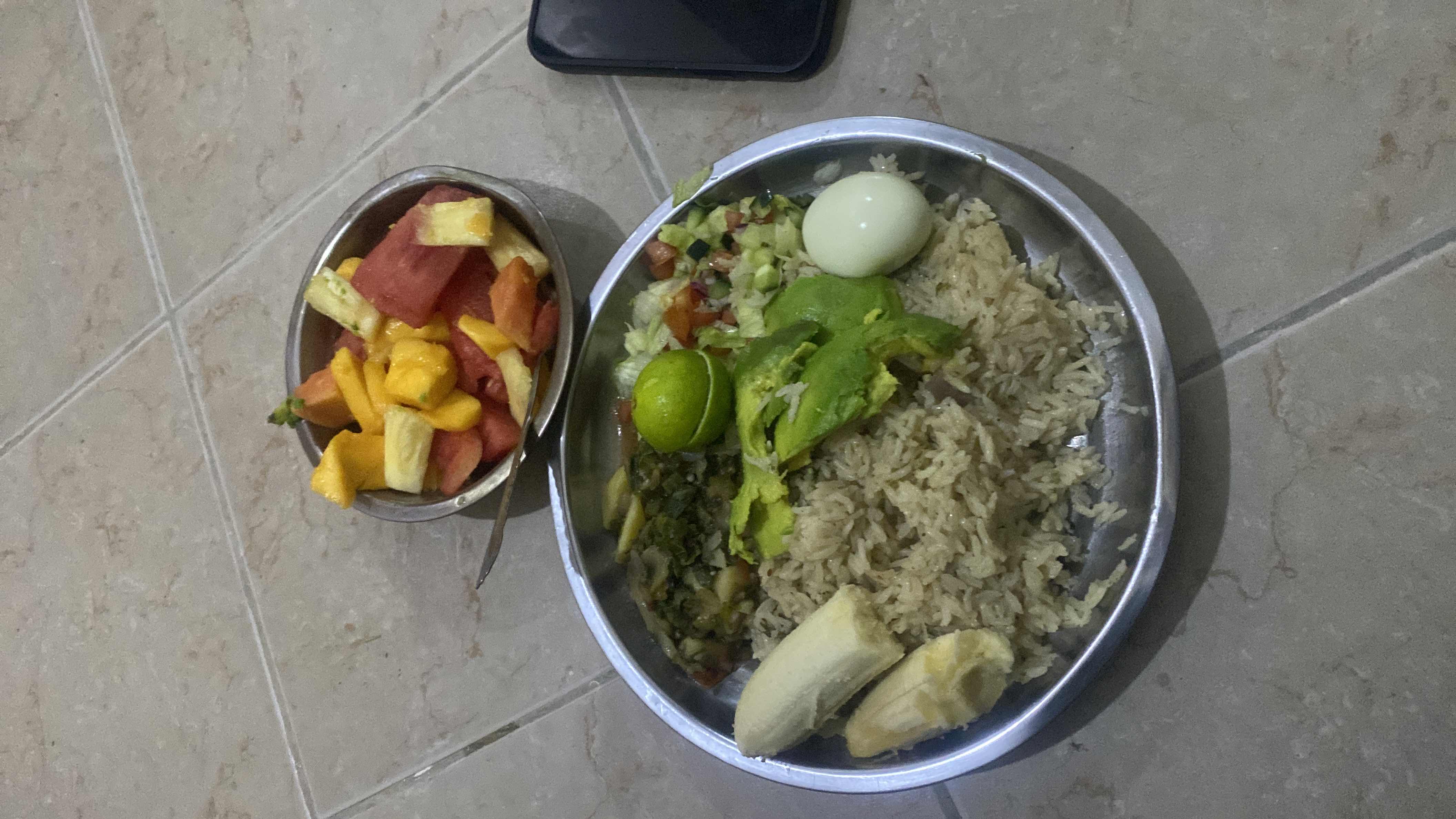 A balanced meal consisting of rice, avocado, boiled egg, banana, mixed vegetables, and a fruit salad.