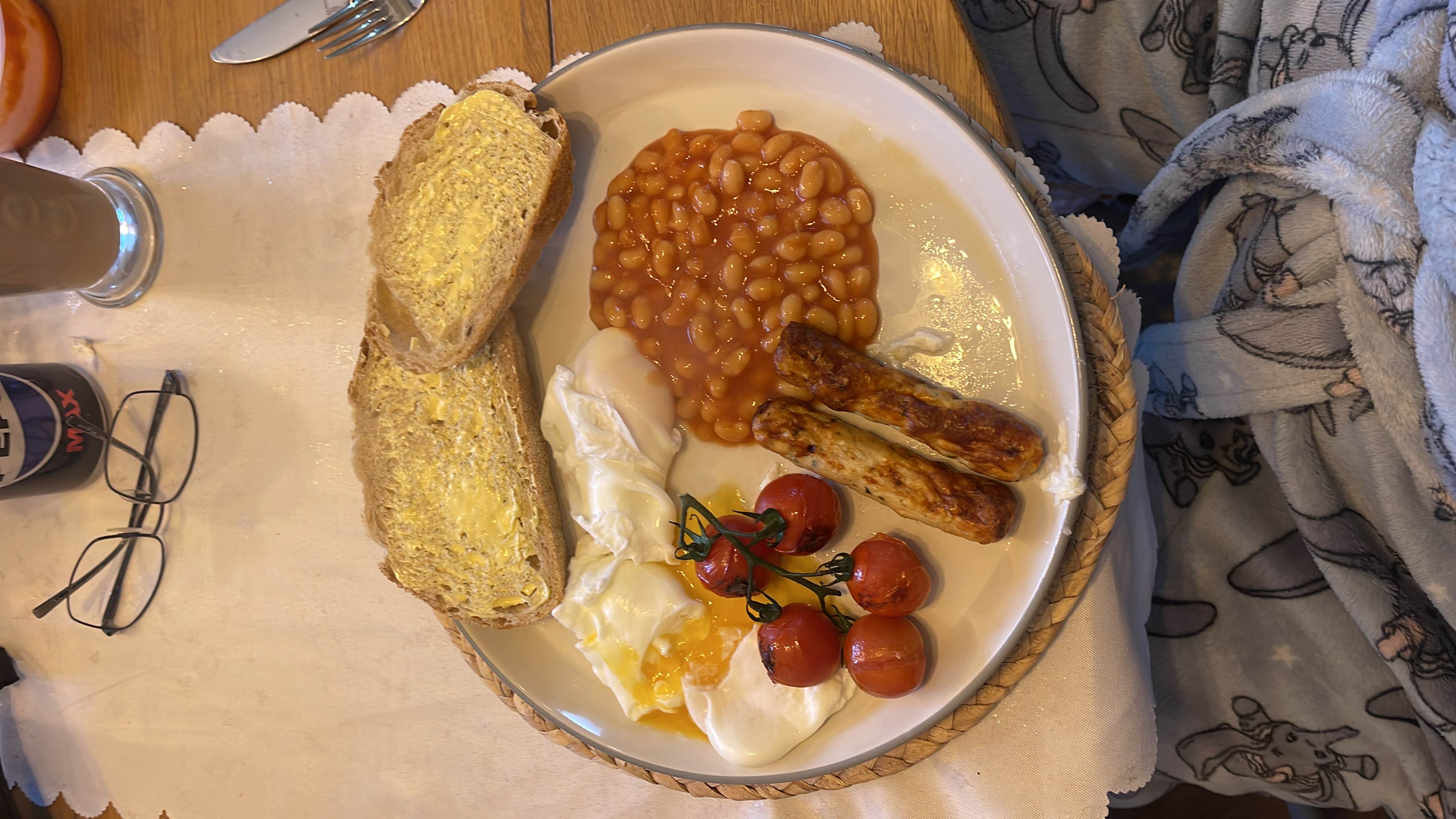 A breakfast with five grilled cherry tomatoes, 2 Heck chickens chipolata sausages, three spoons of baked beans, two poached eggs, and two slices of bread with reduced fat butter.