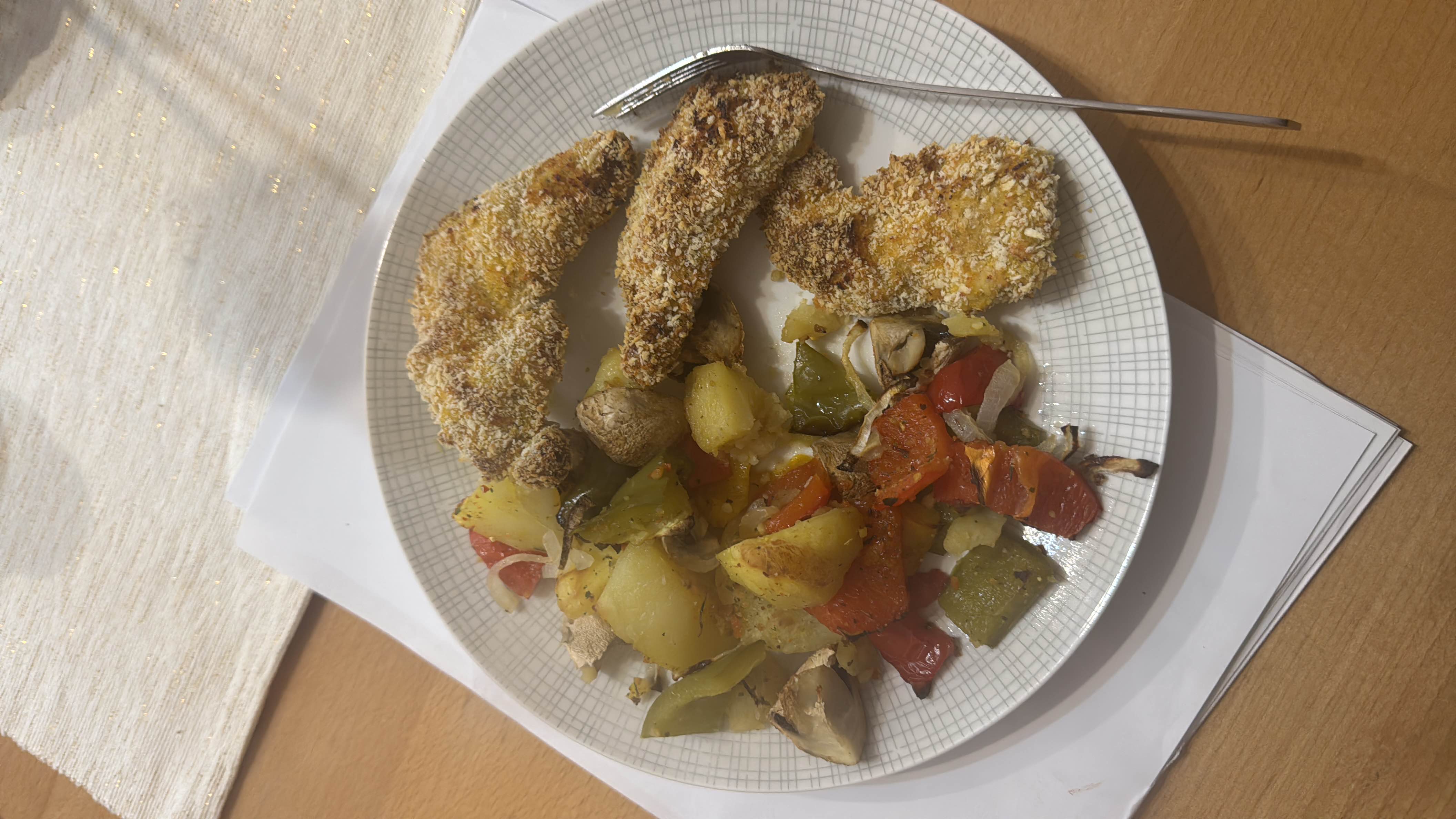 A balanced meal consisting of breaded chicken breast, roasted potatoes, and mixed vegetables including bell peppers and mushrooms.