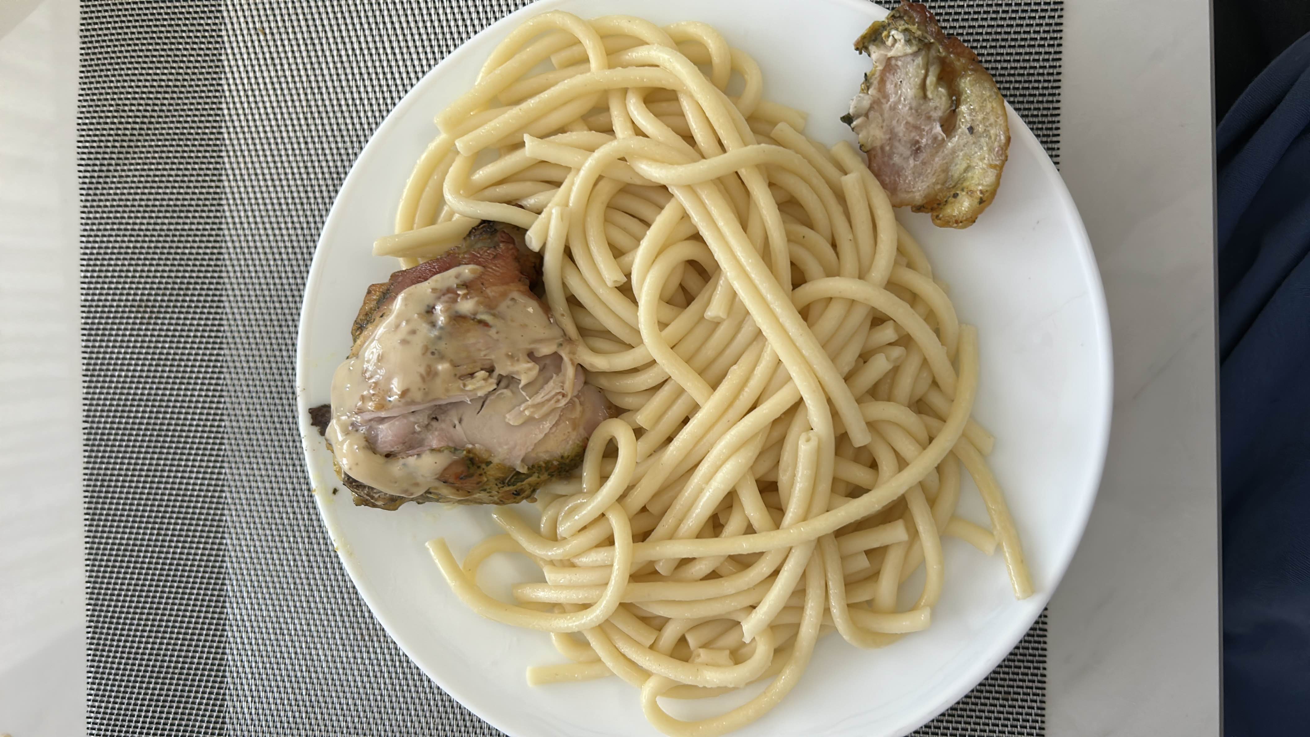 A plate of pasta served with a piece of roasted chicken and a creamy sauce.