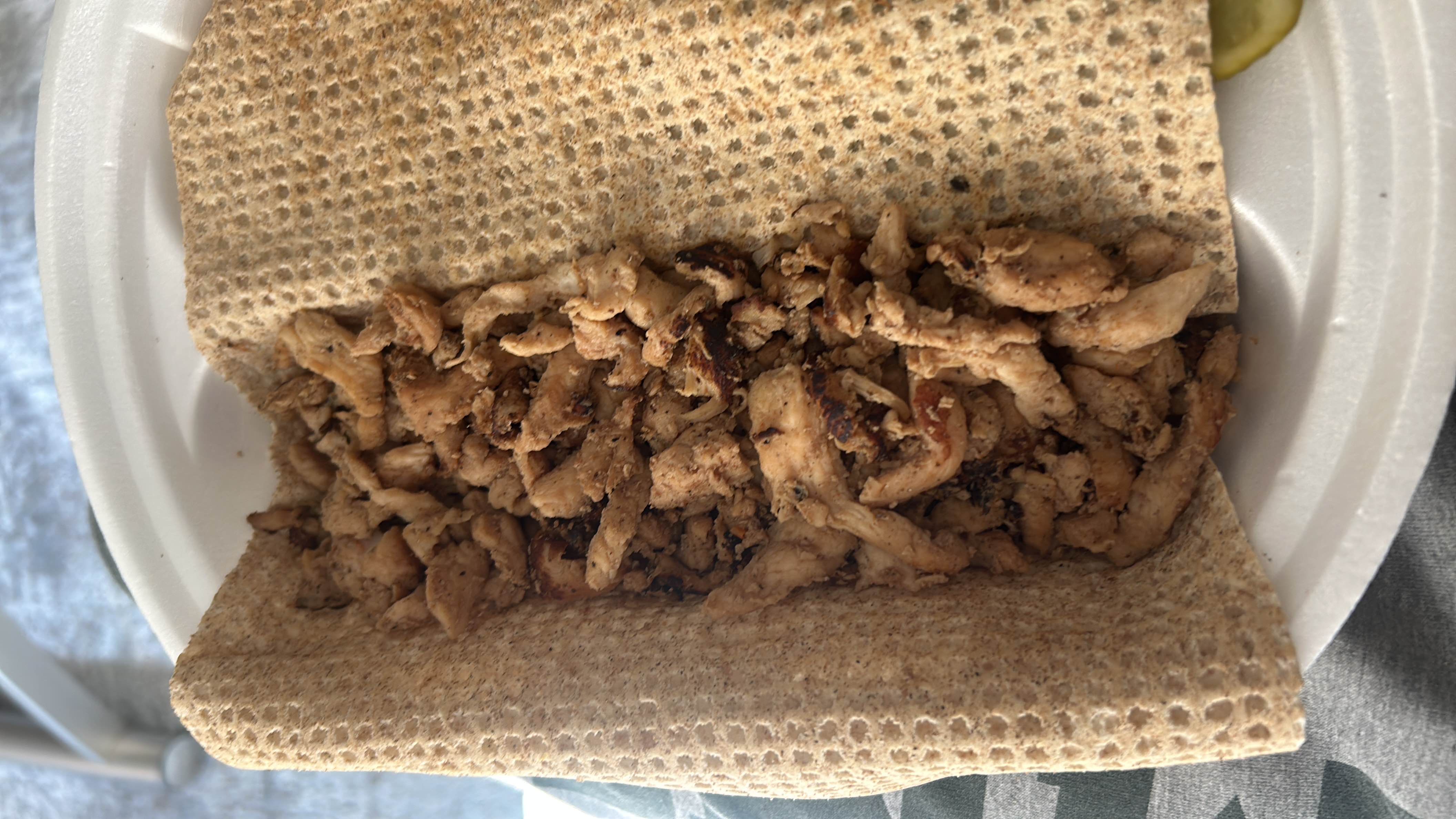 A dish consisting of seasoned chicken wrapped in a whole-grain flatbread, served with a side of pickles.