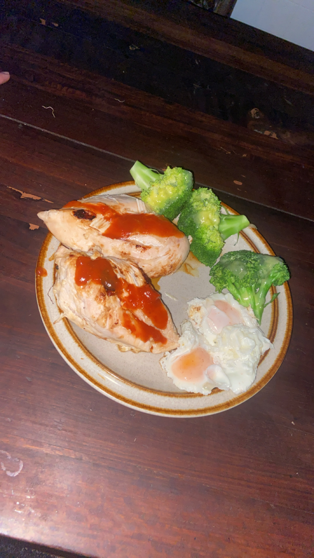 A plate containing two grilled chicken breasts with sauce, two fried eggs, and steamed broccoli, offering a high-protein, low-carb meal.