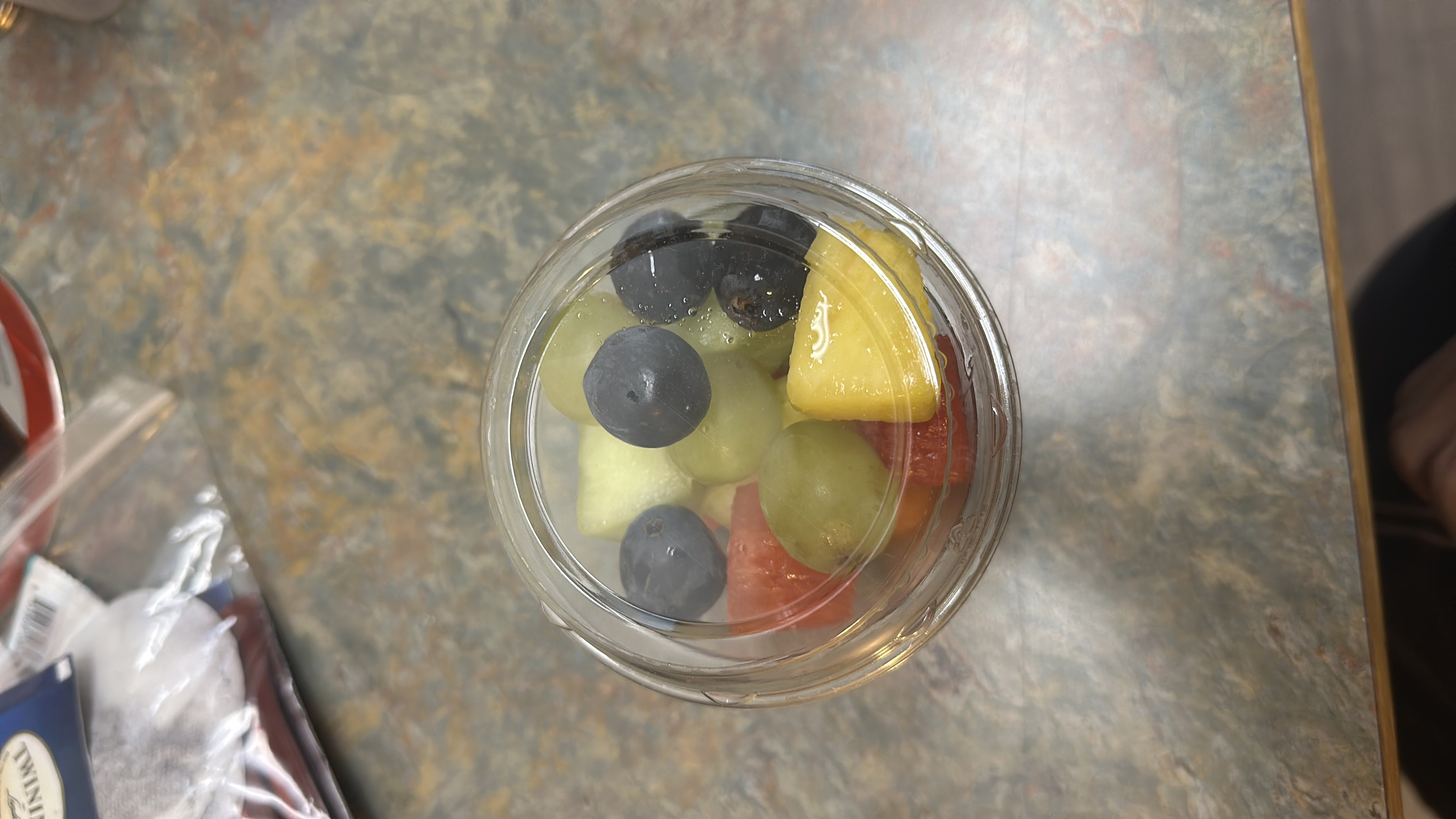 A fresh fruit cup containing blueberries, grapes, pineapple, and watermelon, offering a healthy and low-calorie snack option.