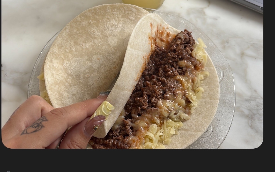 A tortilla wrap with two tortillas, ground beef, melted cheese, savory sauce, and a banana.