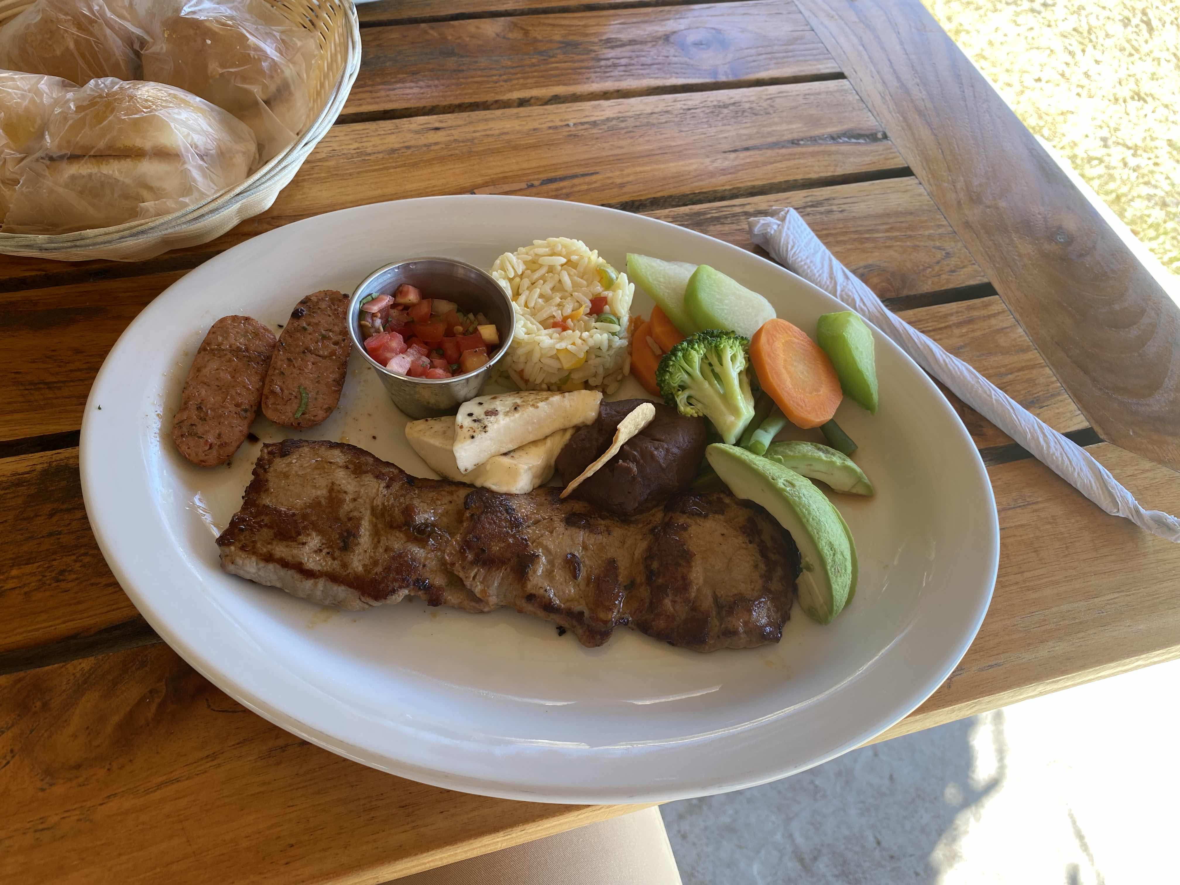 A balanced meal consisting of steak, sausage, vegetables, rice, and bread, providing a mix of protein, carbs, and fats.