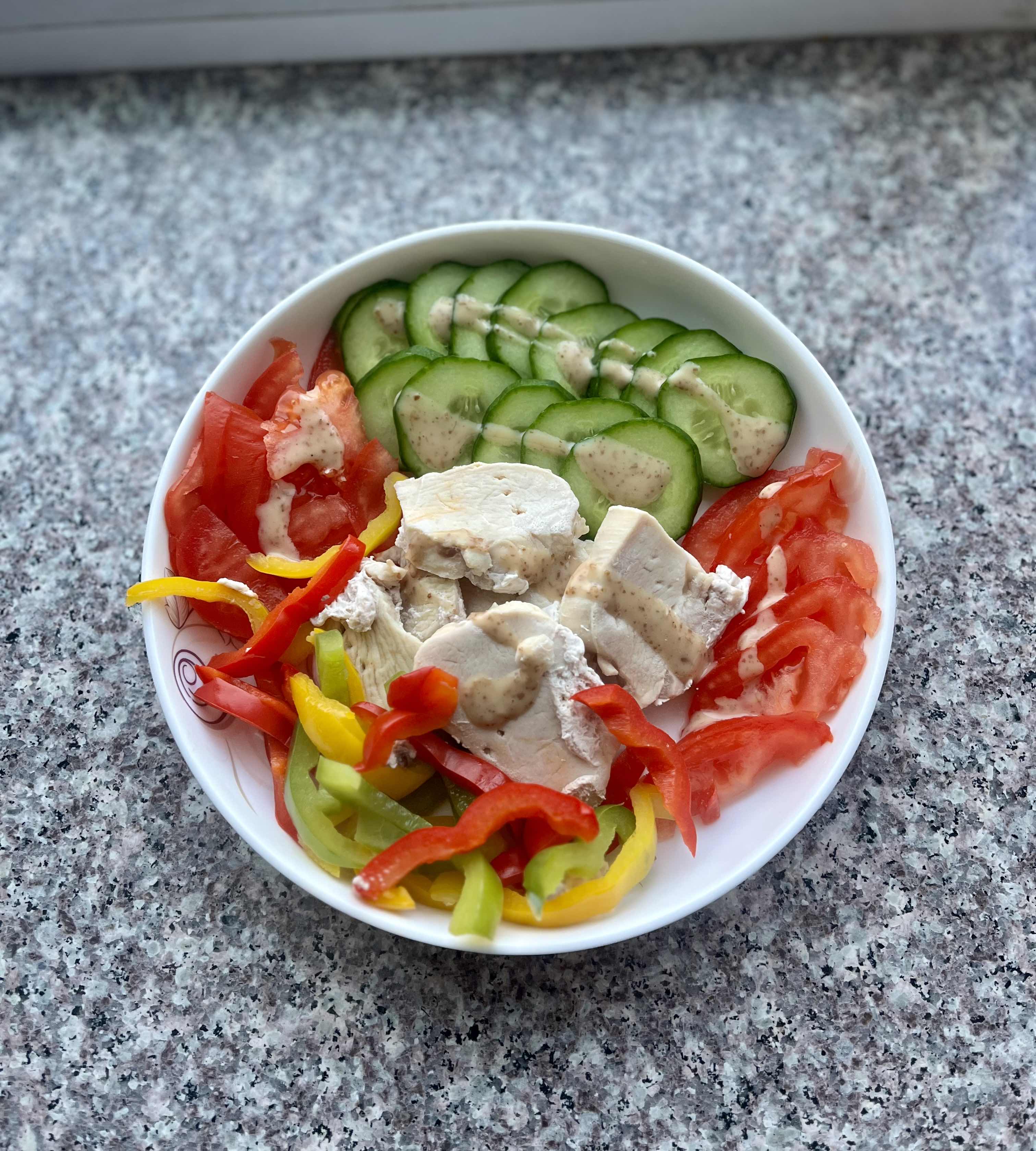 A healthy salad bowl containing chicken breast, cucumber, tomato, bell peppers, and a light dressing.