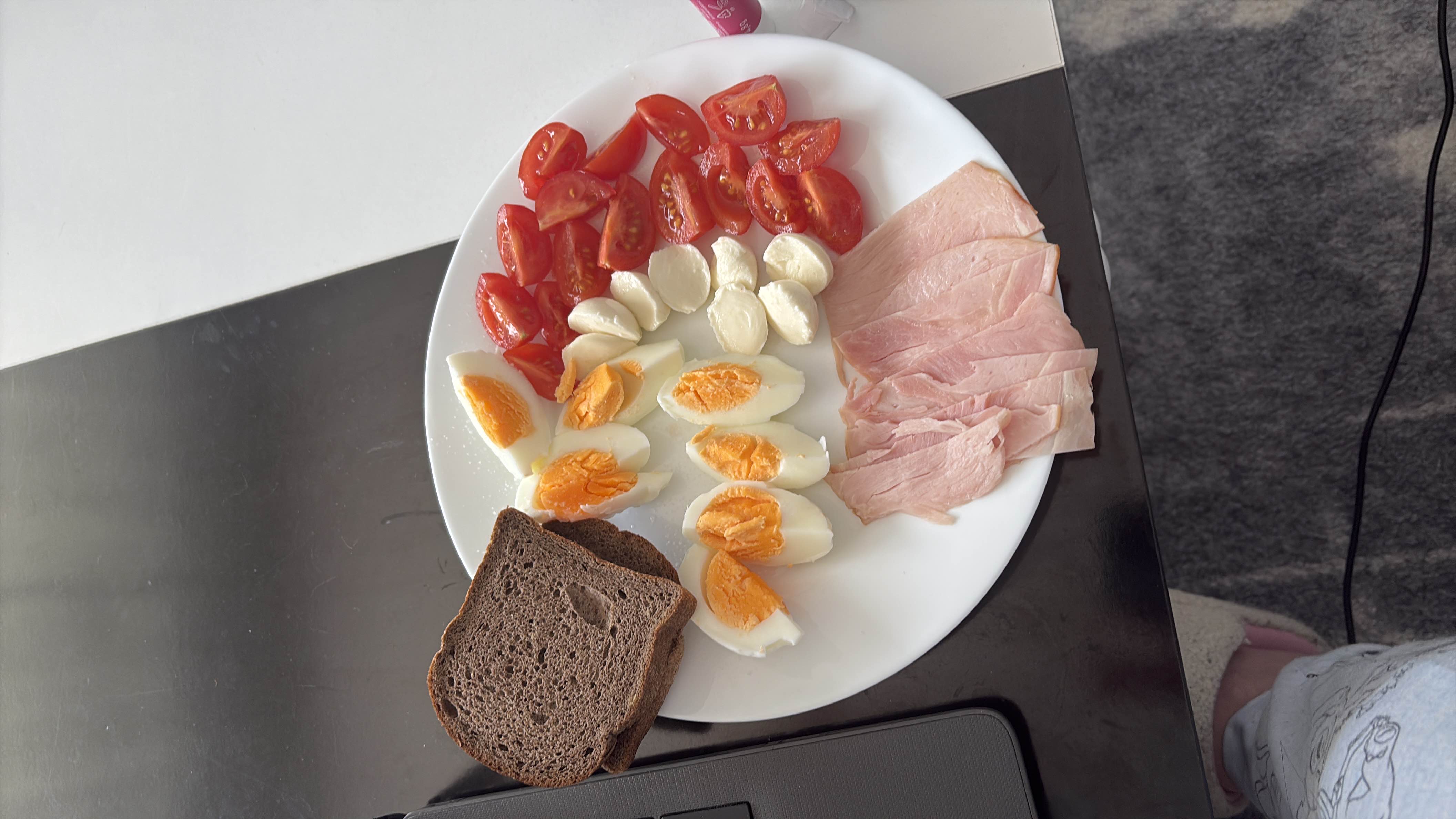 A balanced plate consisting of boiled eggs, cherry tomatoes, mozzarella cheese, ham slices, and rye bread, providing a mix of protein, carbs, and fats.
