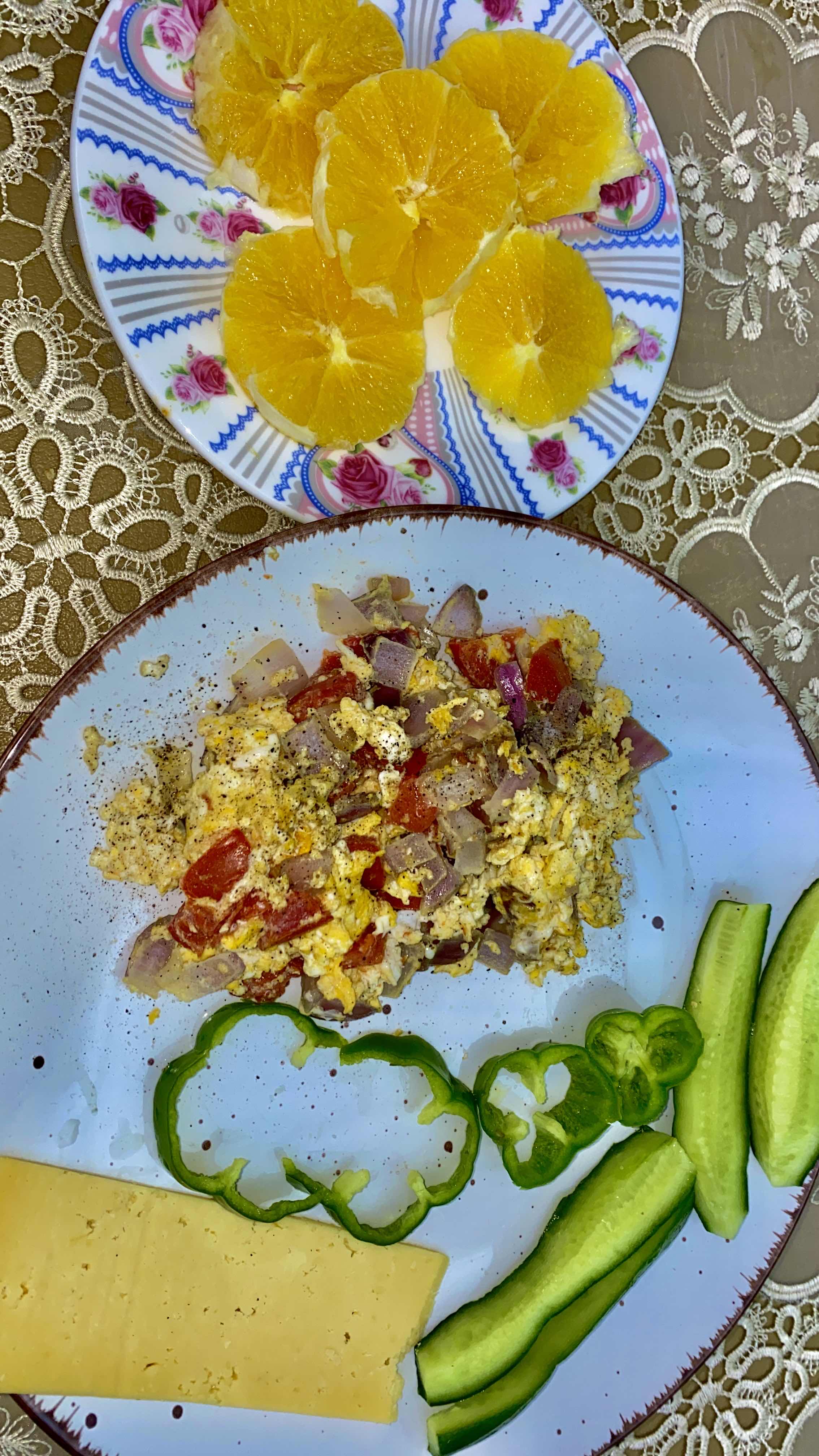 A balanced meal consisting of scrambled eggs with vegetables, cheese, fresh cucumber slices, bell pepper, and orange slices.