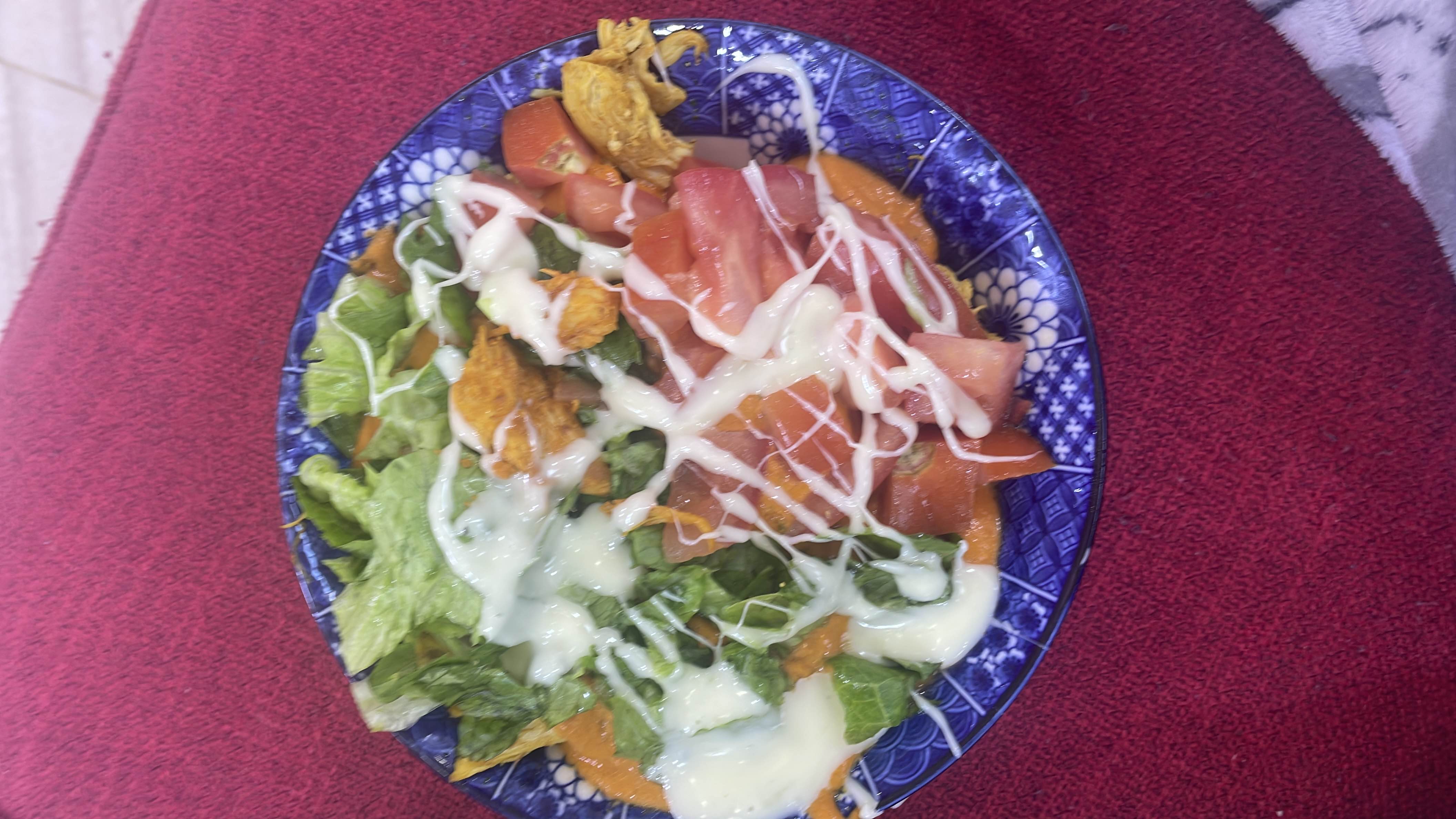 A fresh salad with lettuce, tomato, chicken, tortilla chips, and a creamy dressing.