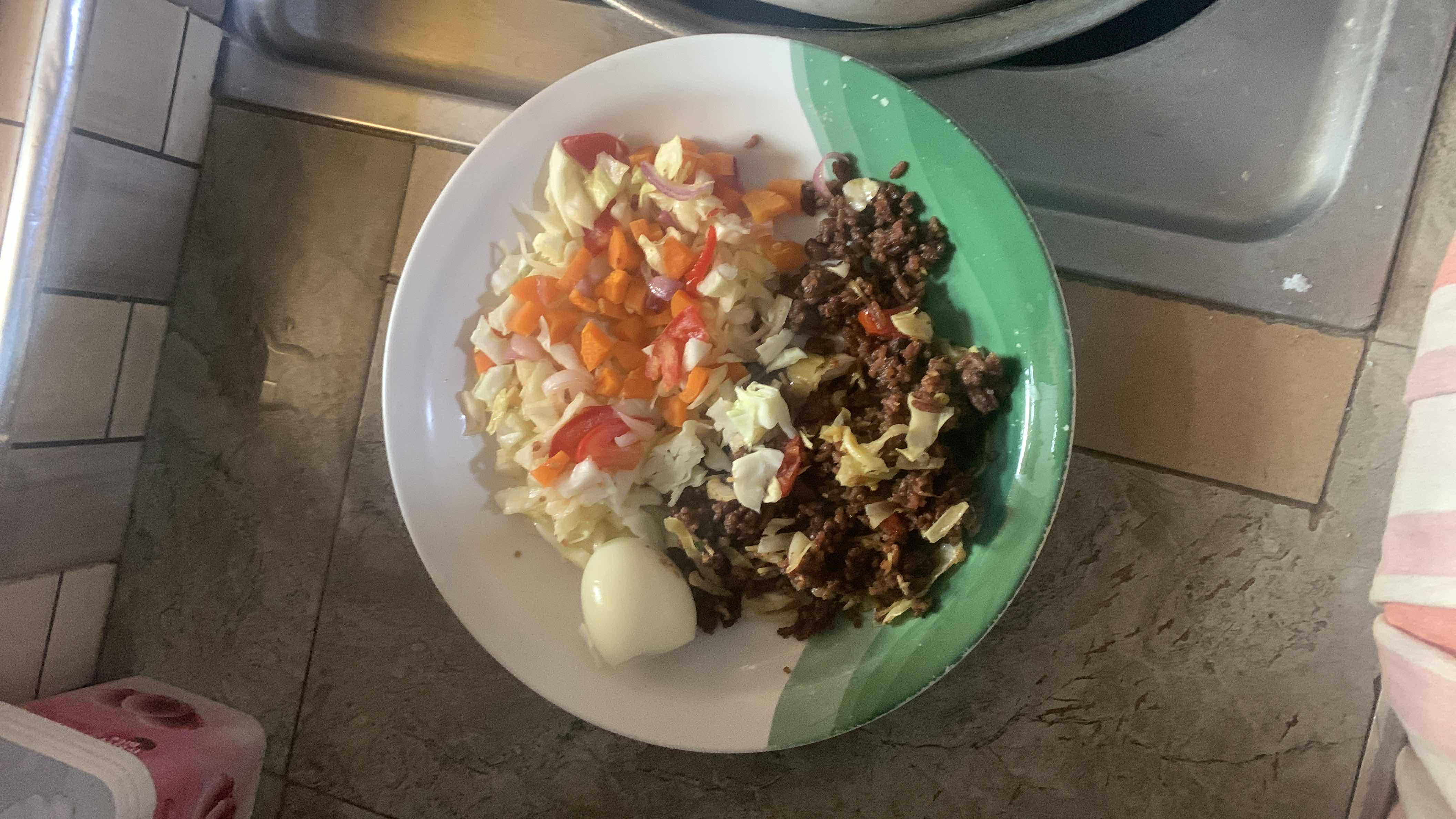 A balanced meal consisting of boiled egg, ground beef, and a mix of vegetables including cabbage, carrots, tomatoes, and onions.